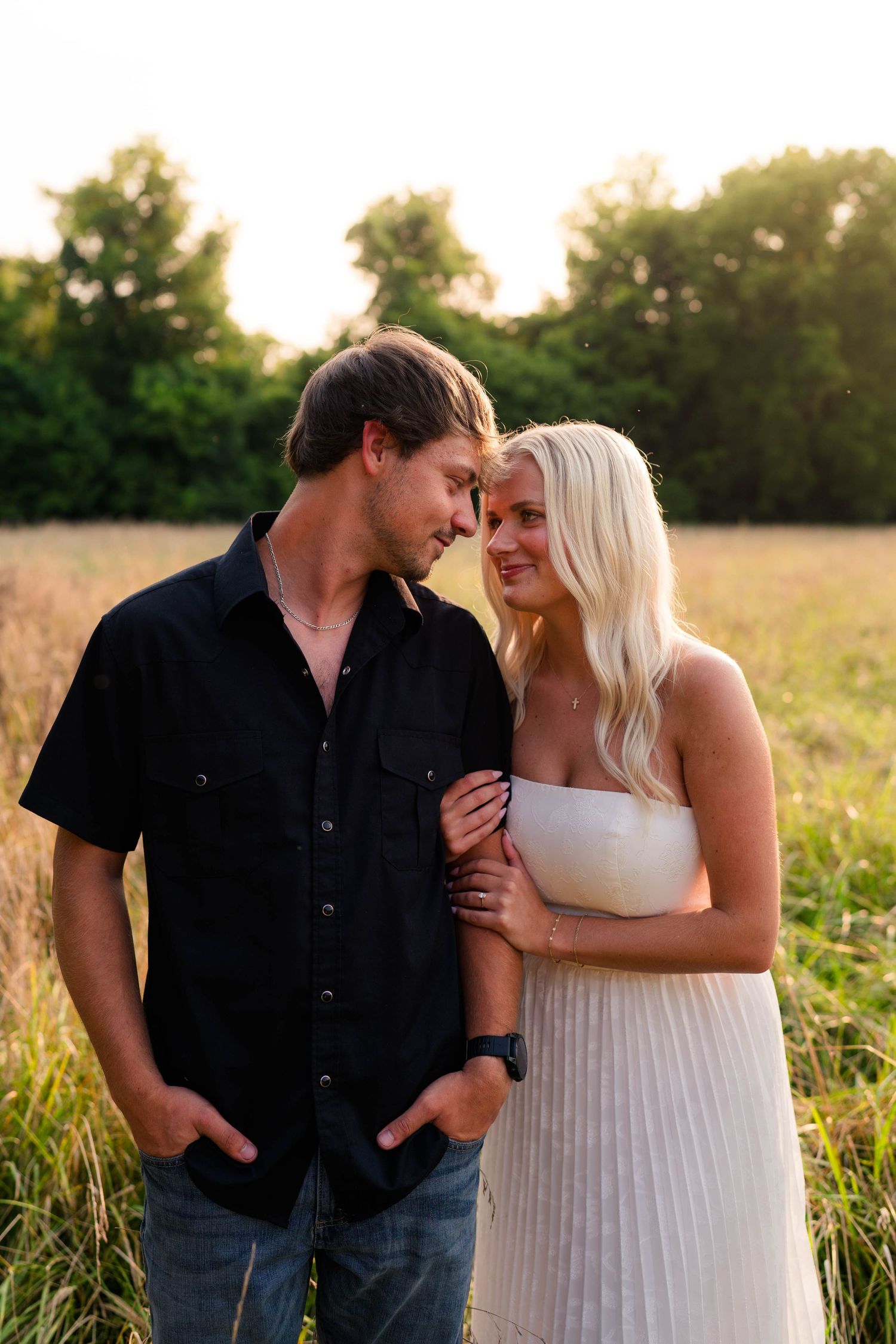 Couple sharing a romantic moment in a golden field at sunset, man in black shirt and woman in white dress.