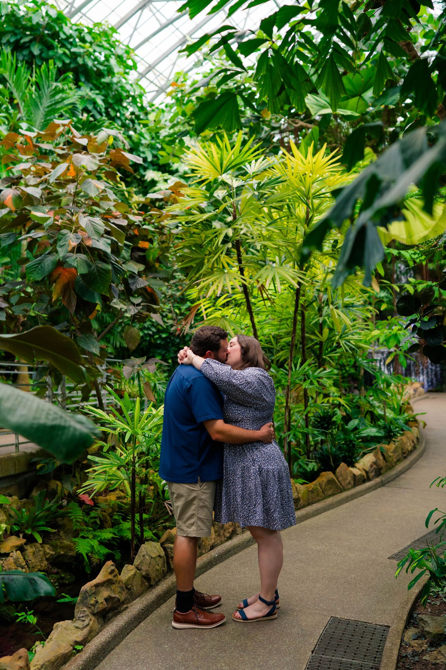 Romantic couple kissing on a garden path surrounded by lush tropical plants.