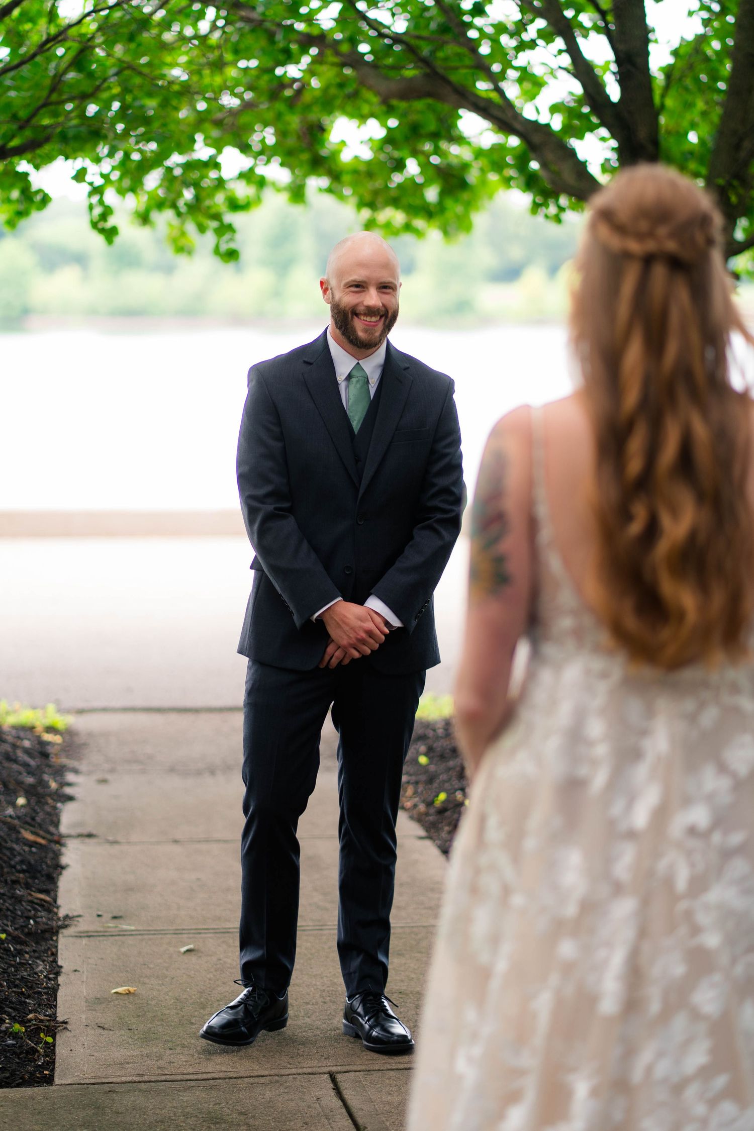 Groom clasping hands smiling joyfully at bride in lace gown during first look.