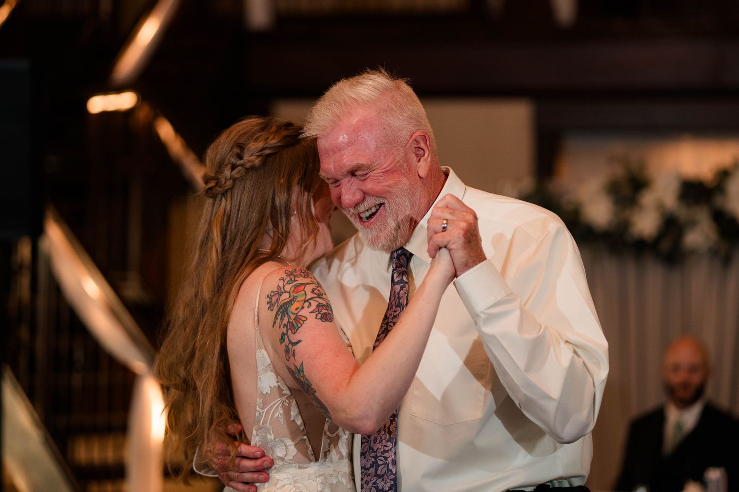 Bride and white-haired father share joyful laugh during father-daughter wedding dance.