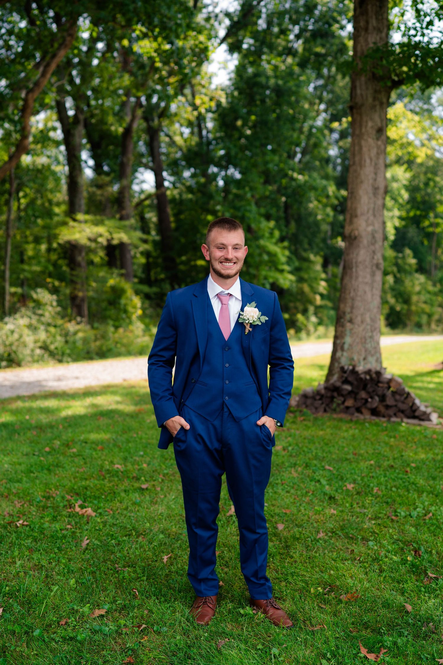 Dapper groom in navy blue three-piece suit with pink tie and boutonniere posing outdoors.