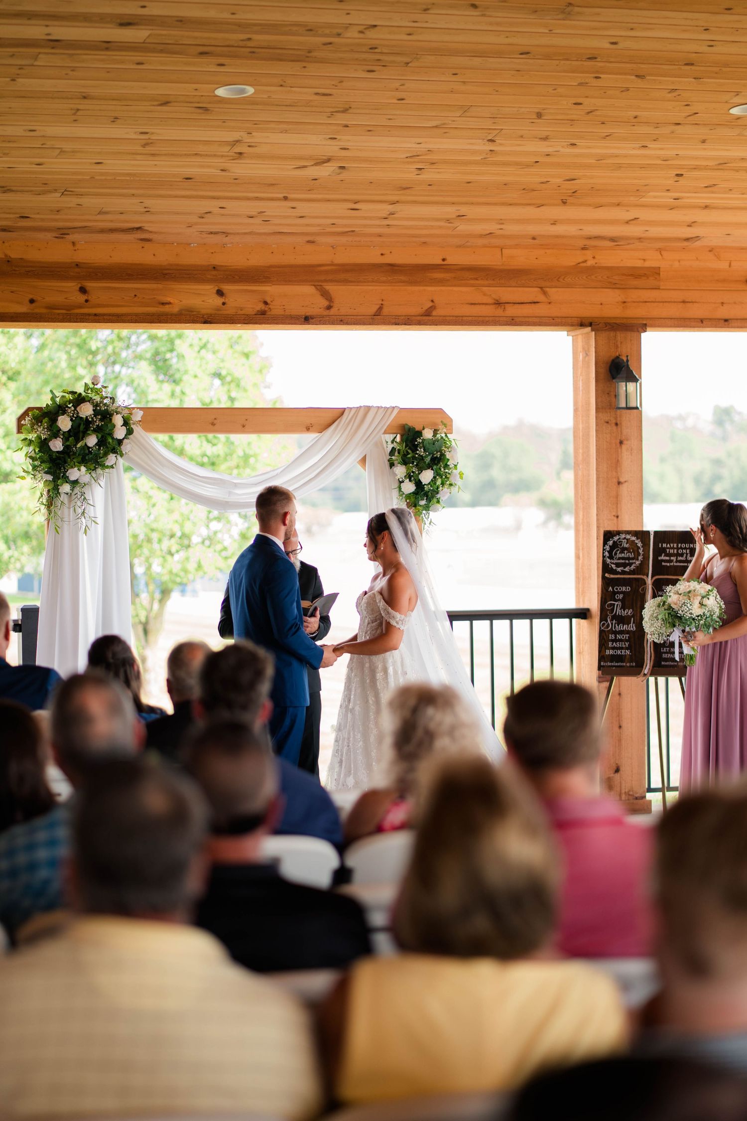 Bride and groom hold hands at altar during wedding ceremony with seated guests watching.