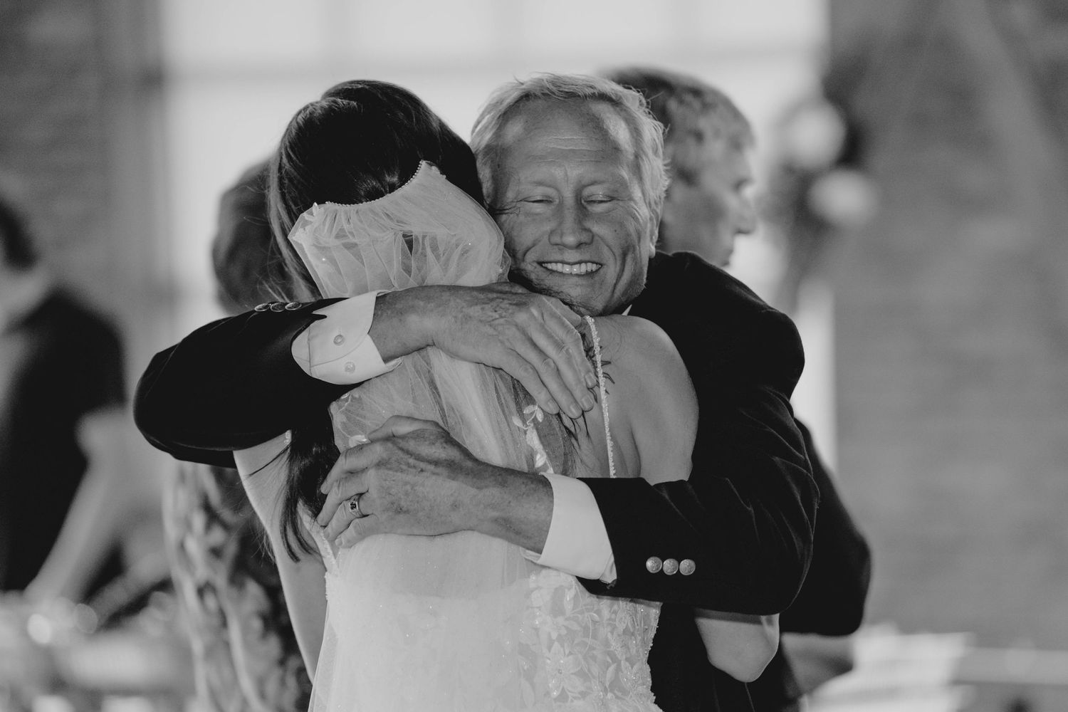 Black and white photo of an emotional father-daughter hug during a wedding reception.