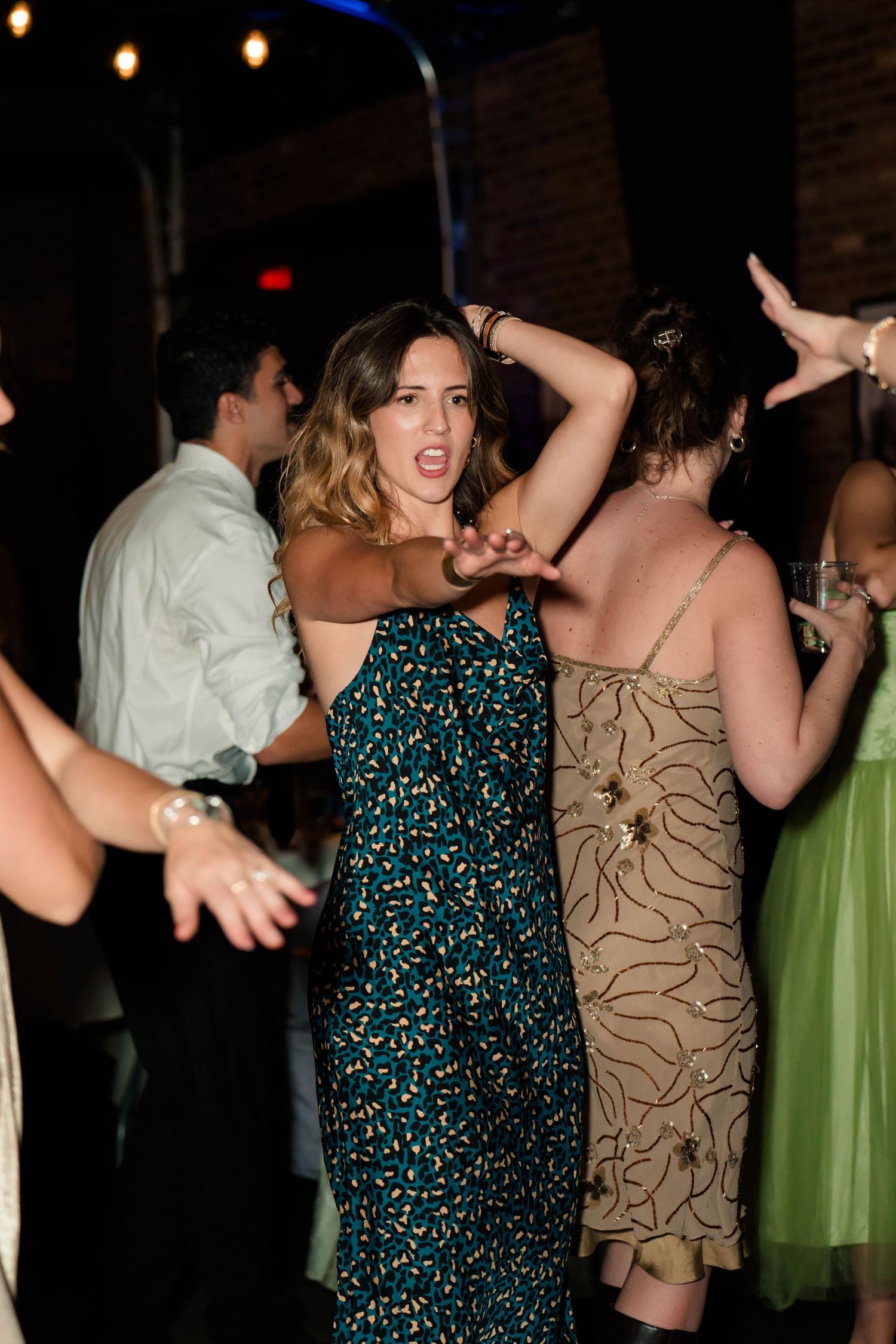 Guest in floral green dress dances energetically at lively wedding reception under string lights.
