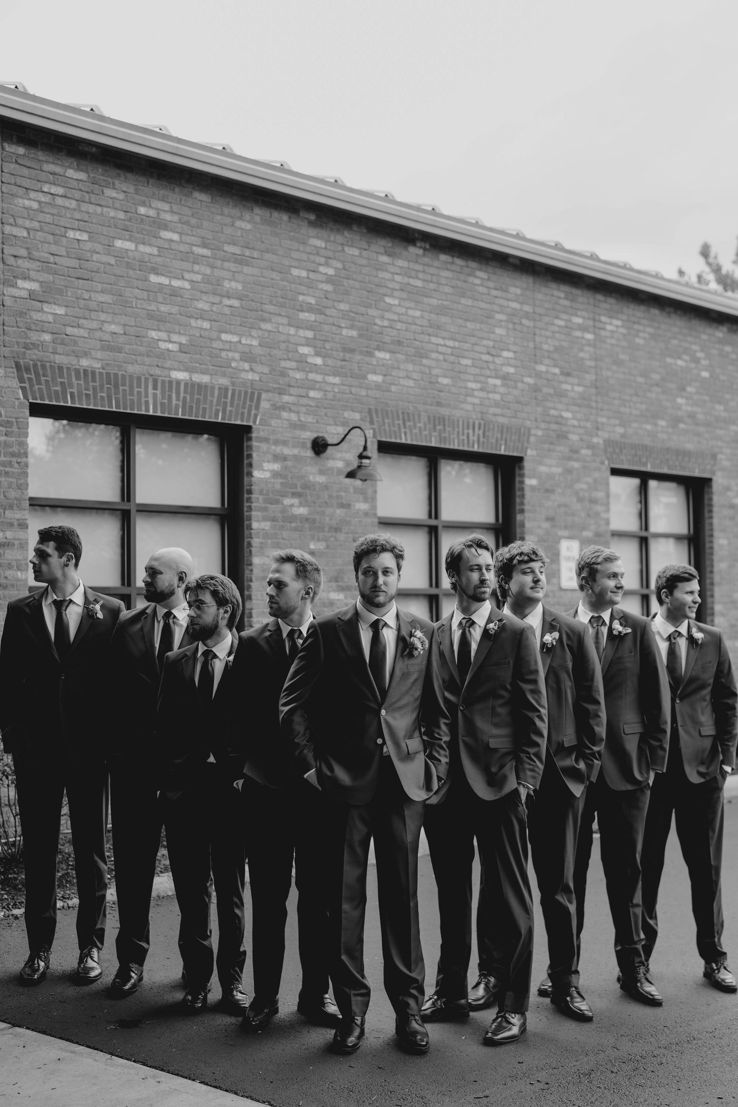 Black and white photo of groomsmen lined up outside a brick building at wedding.