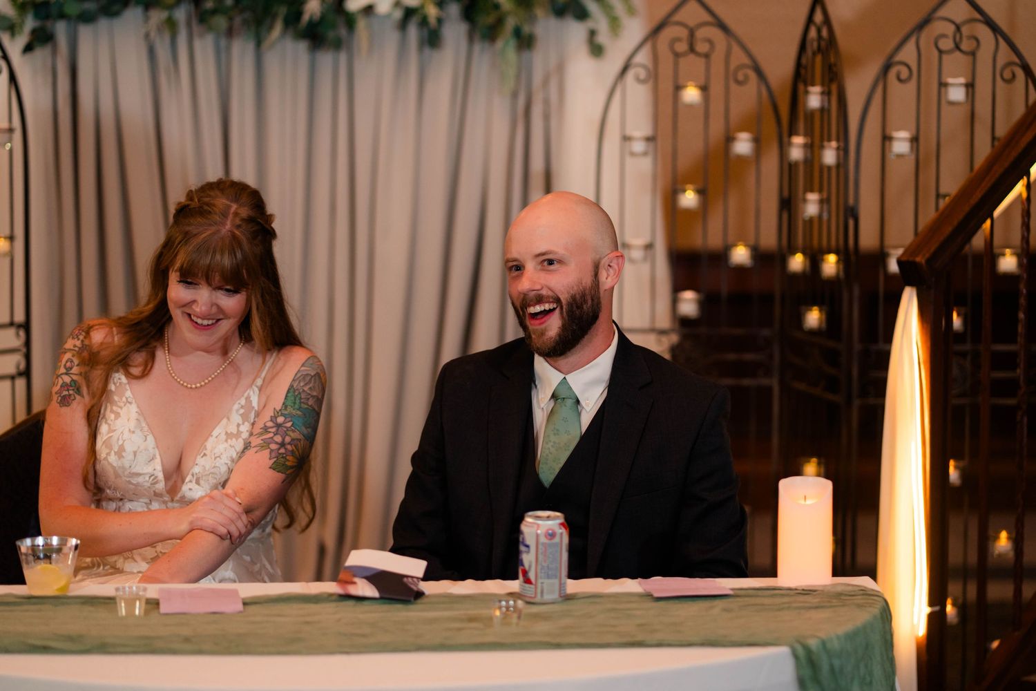 Bride and groom laughing joyfully at sweetheart table during wedding reception.
