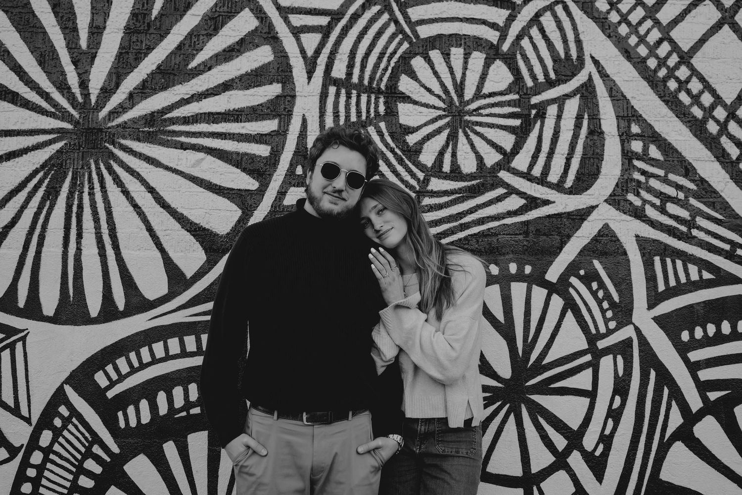 Black and white photo of a couple posing together in front of a bold floral mural.
