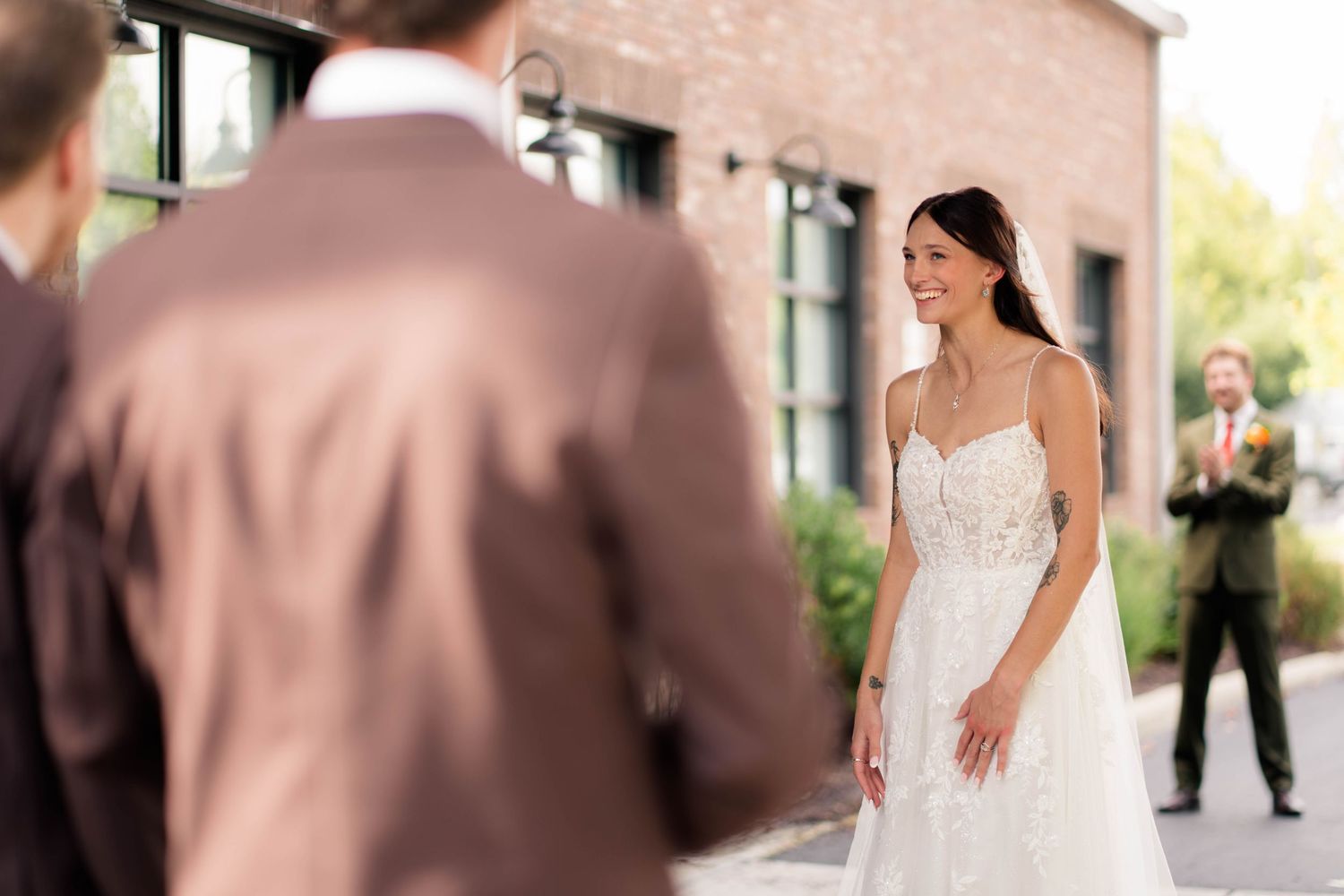 Smiling bride in lace wedding dress during outdoor first look moment at brick venue.