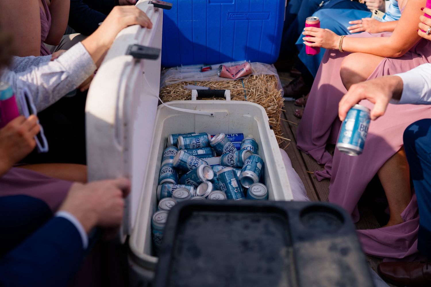 Cooler filled with canned beverages being accessed by wedding guests at outdoor reception.