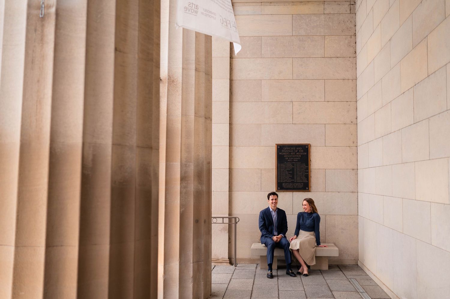 Couple conversing while seated between grand stone columns of a classical architecture building.