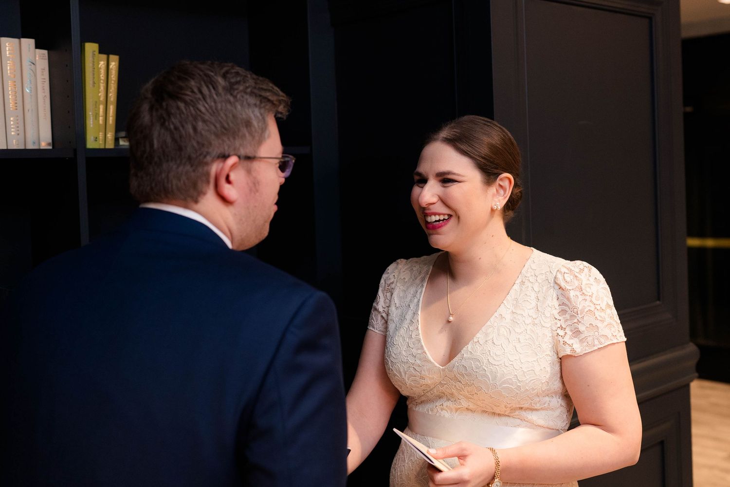 Bride laughing joyfully with groom during intimate wedding vow exchange in elegant dark-paneled venue.
