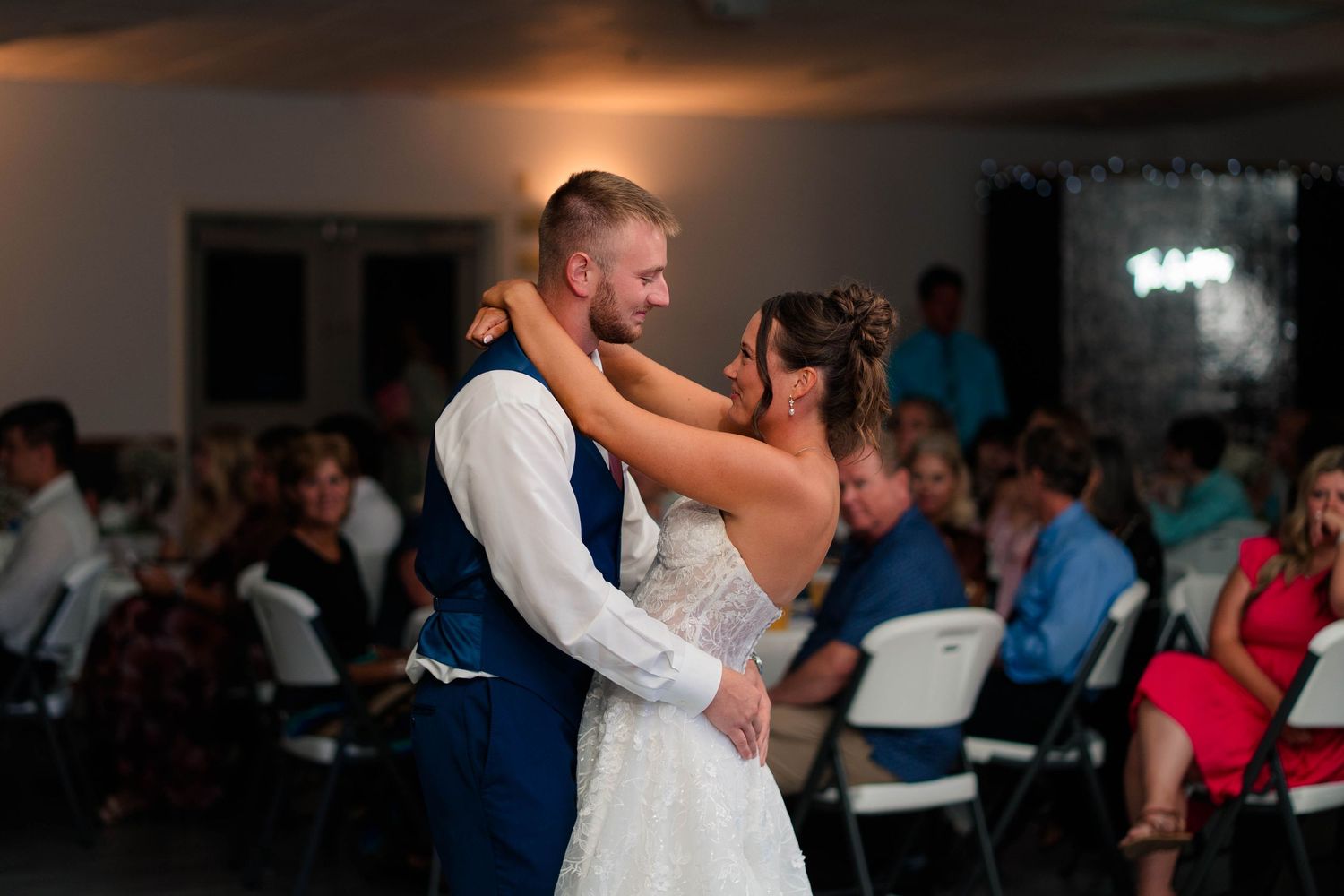 Bride and groom share an intimate first dance moment while guests watch from surrounding tables at the reception.