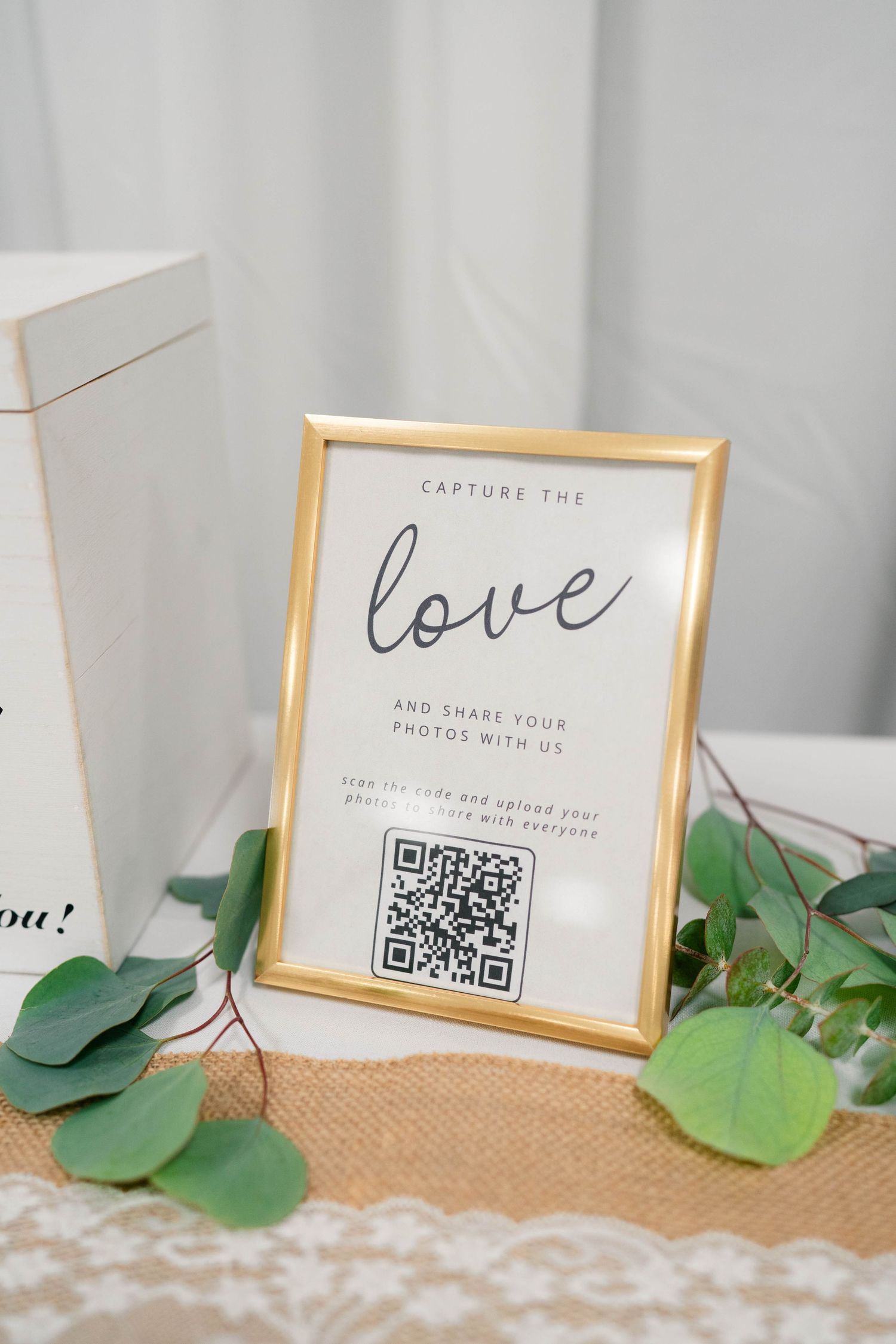 Gold framed wedding sign reading capture the love with QR code on burlap table runner.