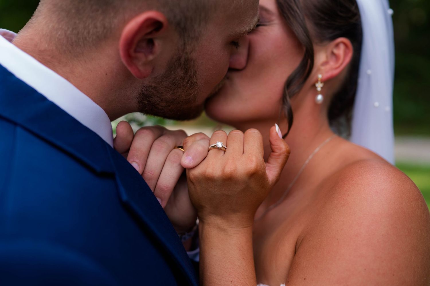 Bride and groom share a romantic kiss while displaying their wedding rings on their wedding day.