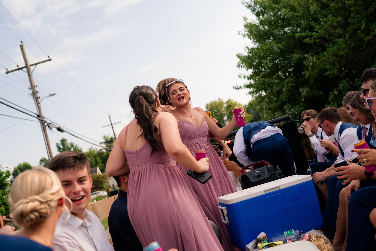 Bridesmaids in mauve dresses laugh and dance joyfully outdoors during a lively wedding celebration event.