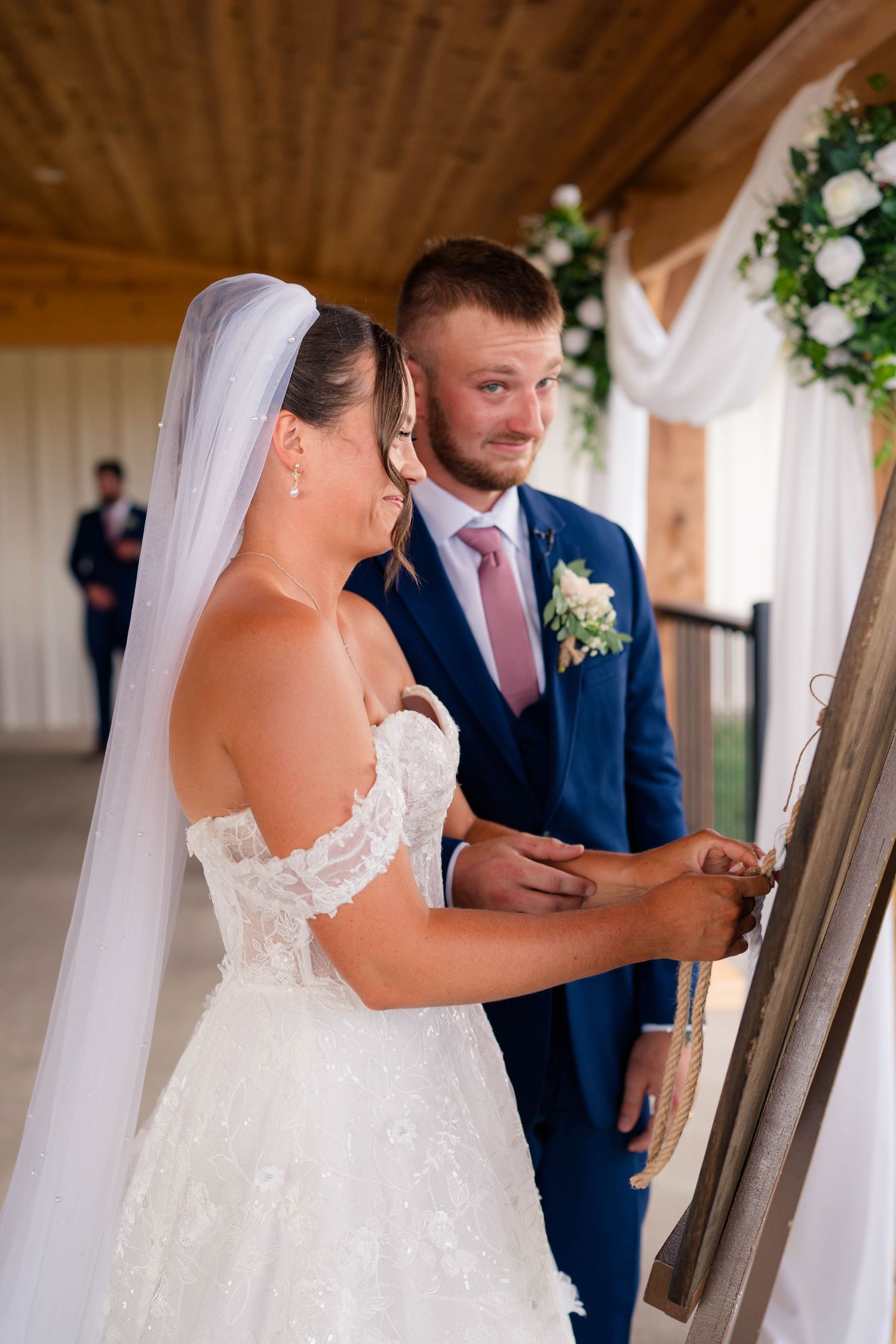 Bride and groom participate in a unity ceremony under wooden pavilion during their wedding.