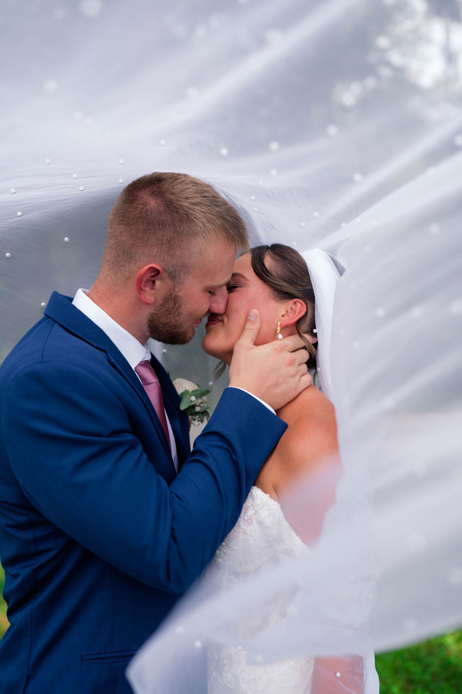 Bride and groom share a romantic kiss under a flowing white veil on their wedding day.
