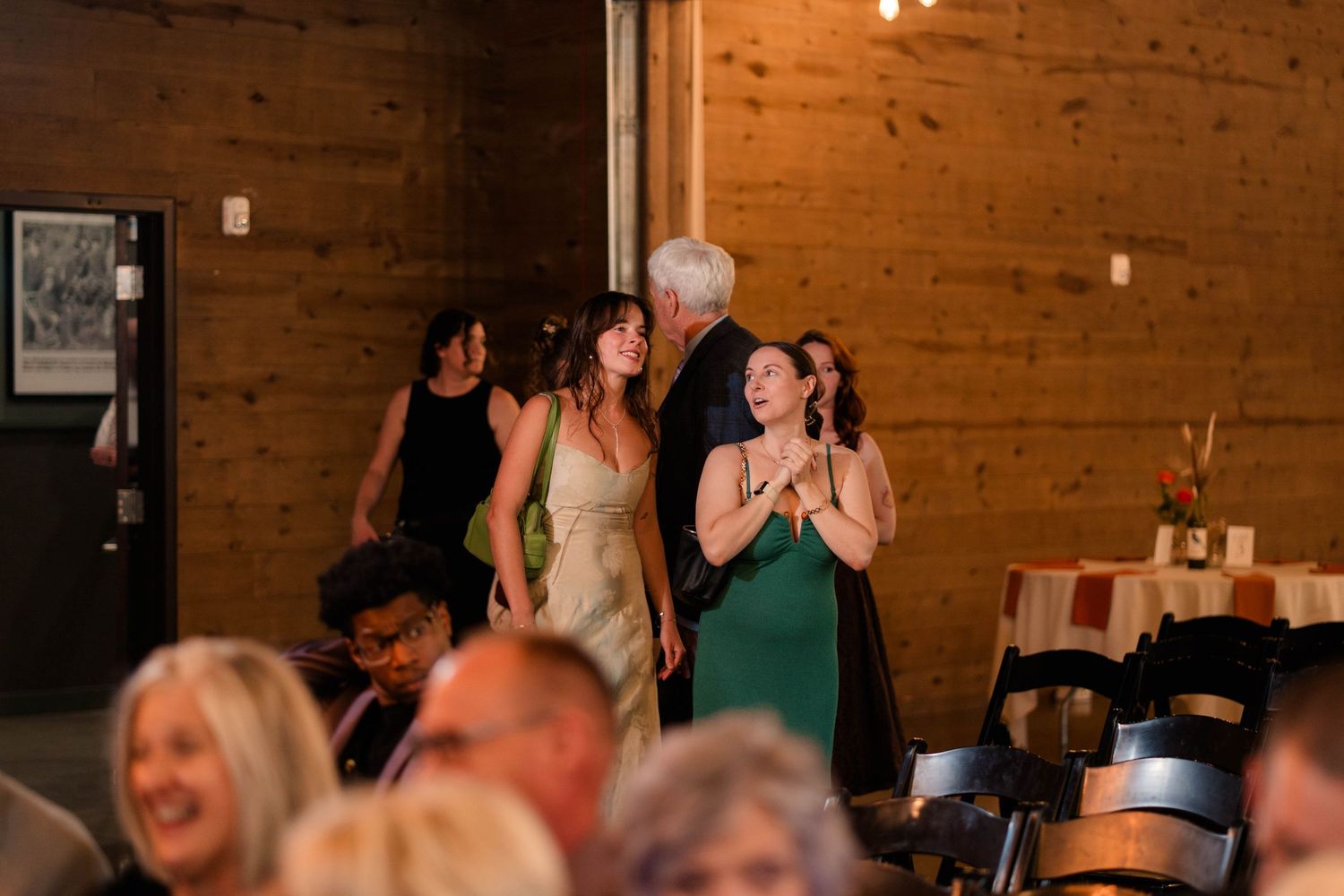 Wedding guests watching a special moment during an indoor reception in a rustic wood-paneled venue.