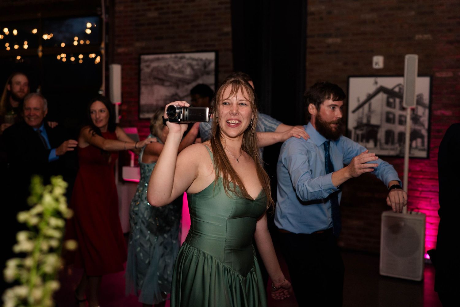 Wedding guest in green dress films reception dancing with handheld camera at lively celebration.