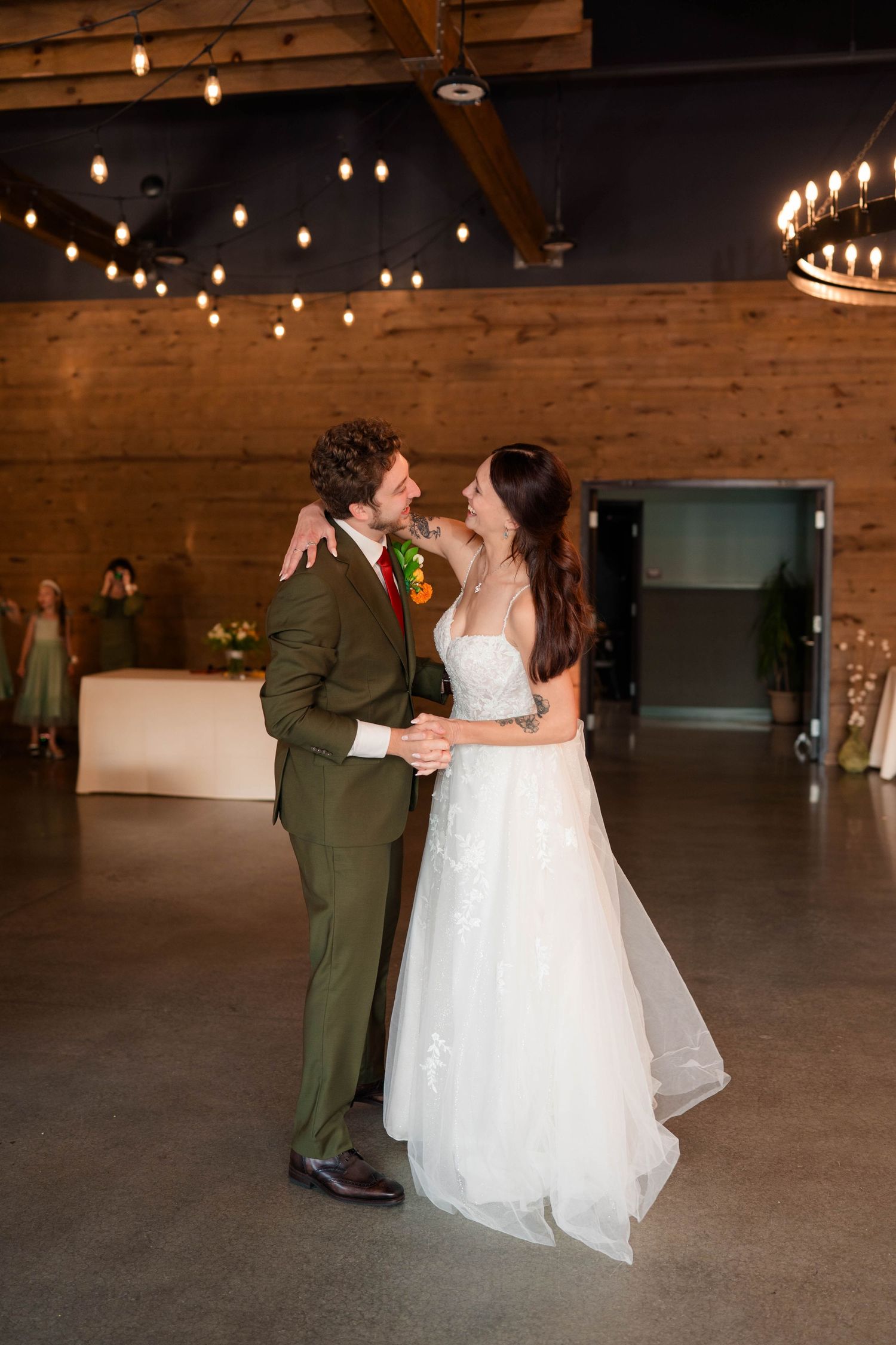 Bride and groom share their first dance under warm string lights in a rustic industrial wedding reception venue.
