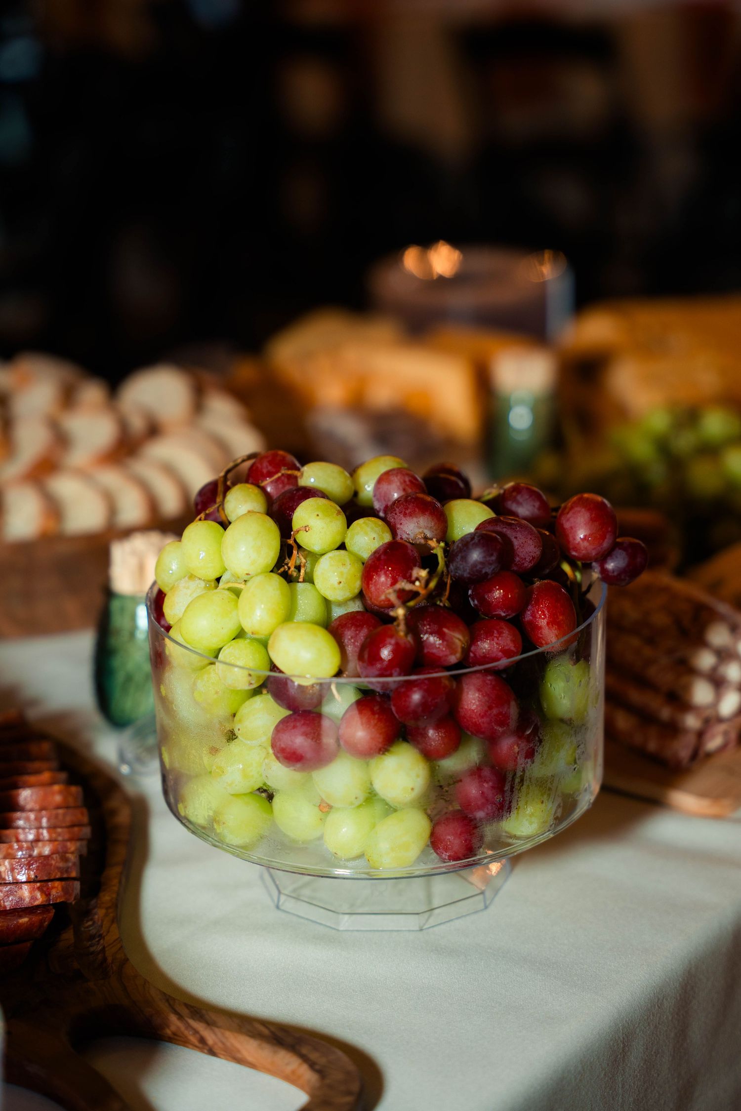 Glass pedestal bowl filled with fresh green and red grapes on wedding charcuterie table.