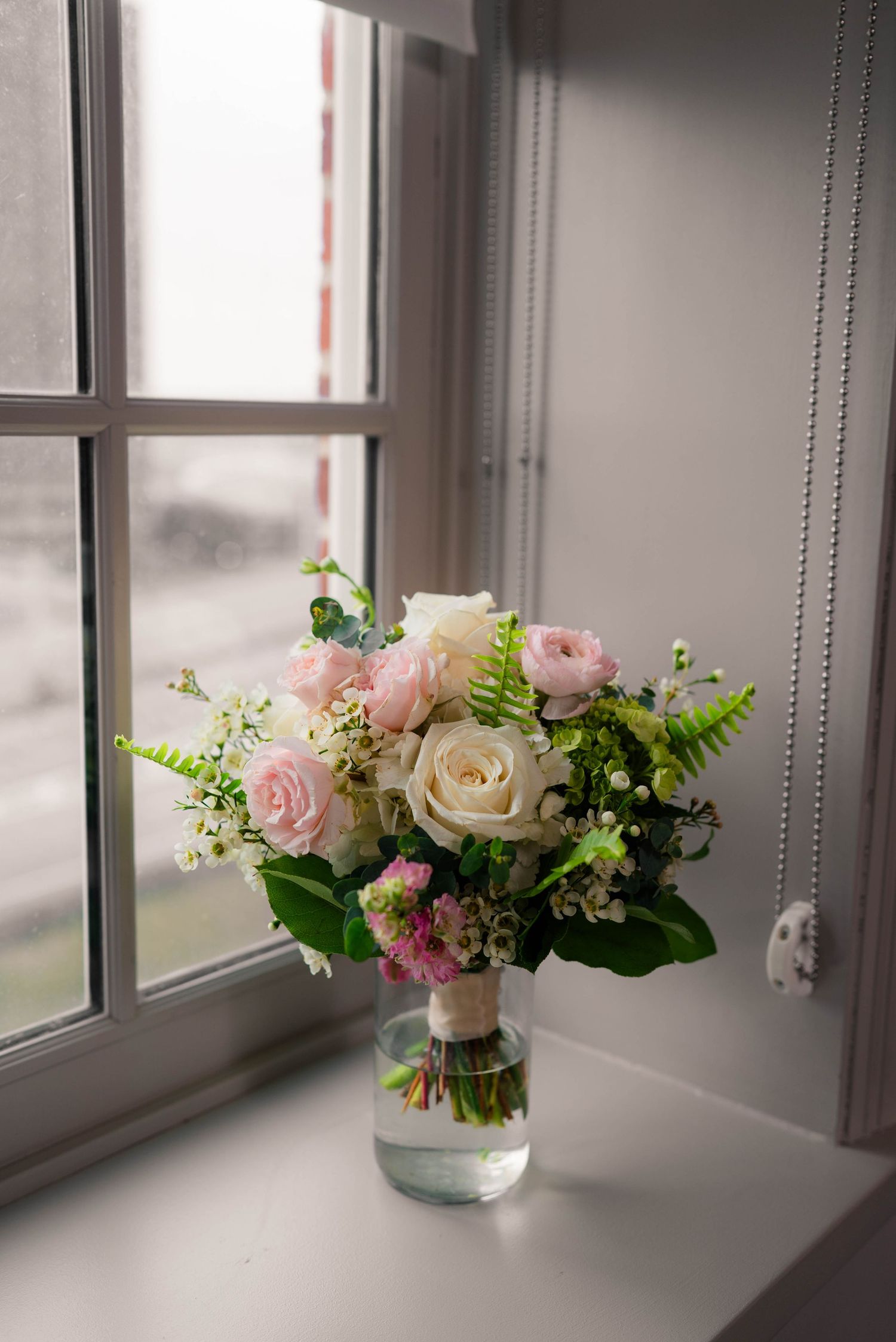 Elegant bridal bouquet with pink and white roses in a vase on a bright windowsill.