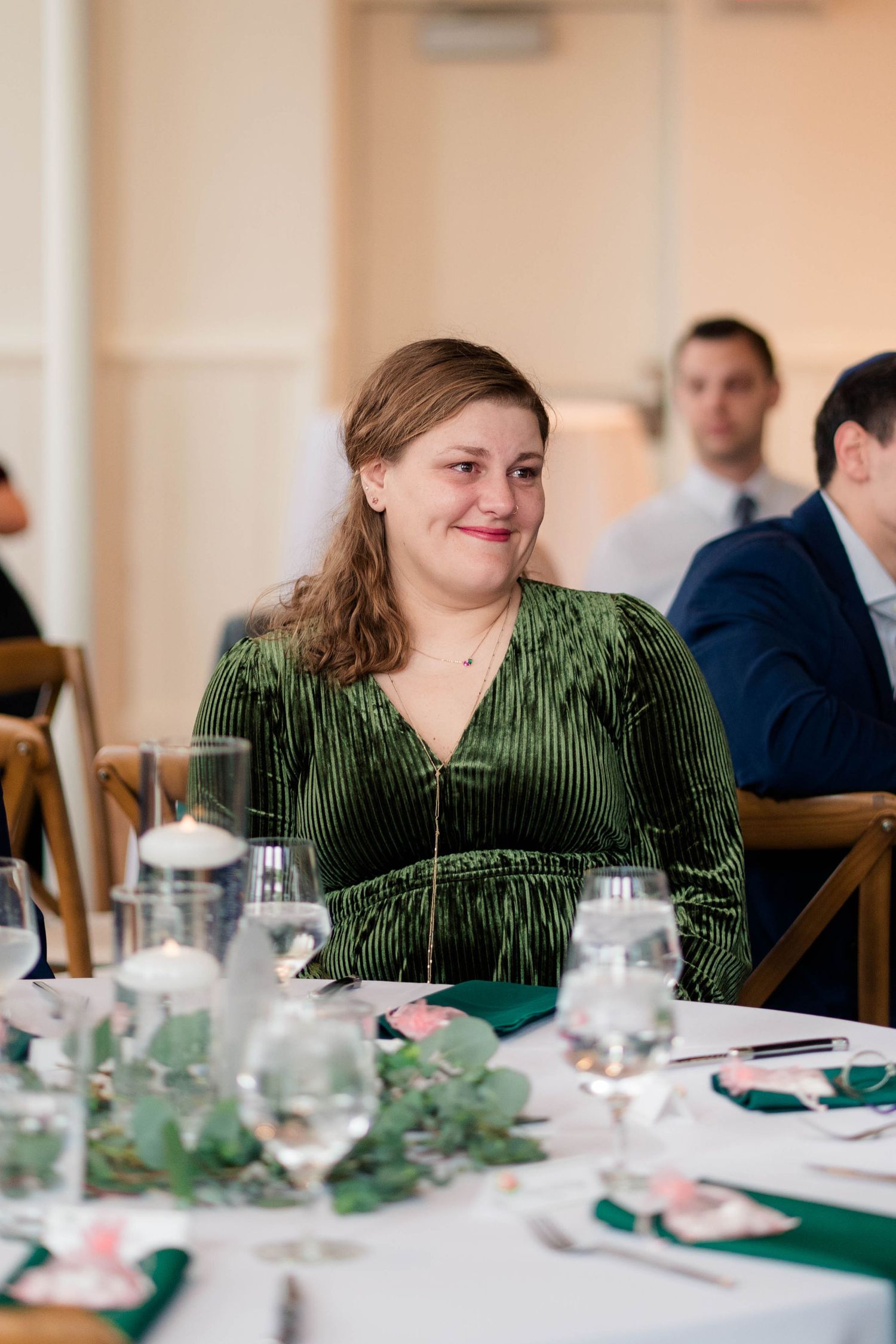 Smiling woman in green velvet dress seated at elegantly decorated wedding reception table.