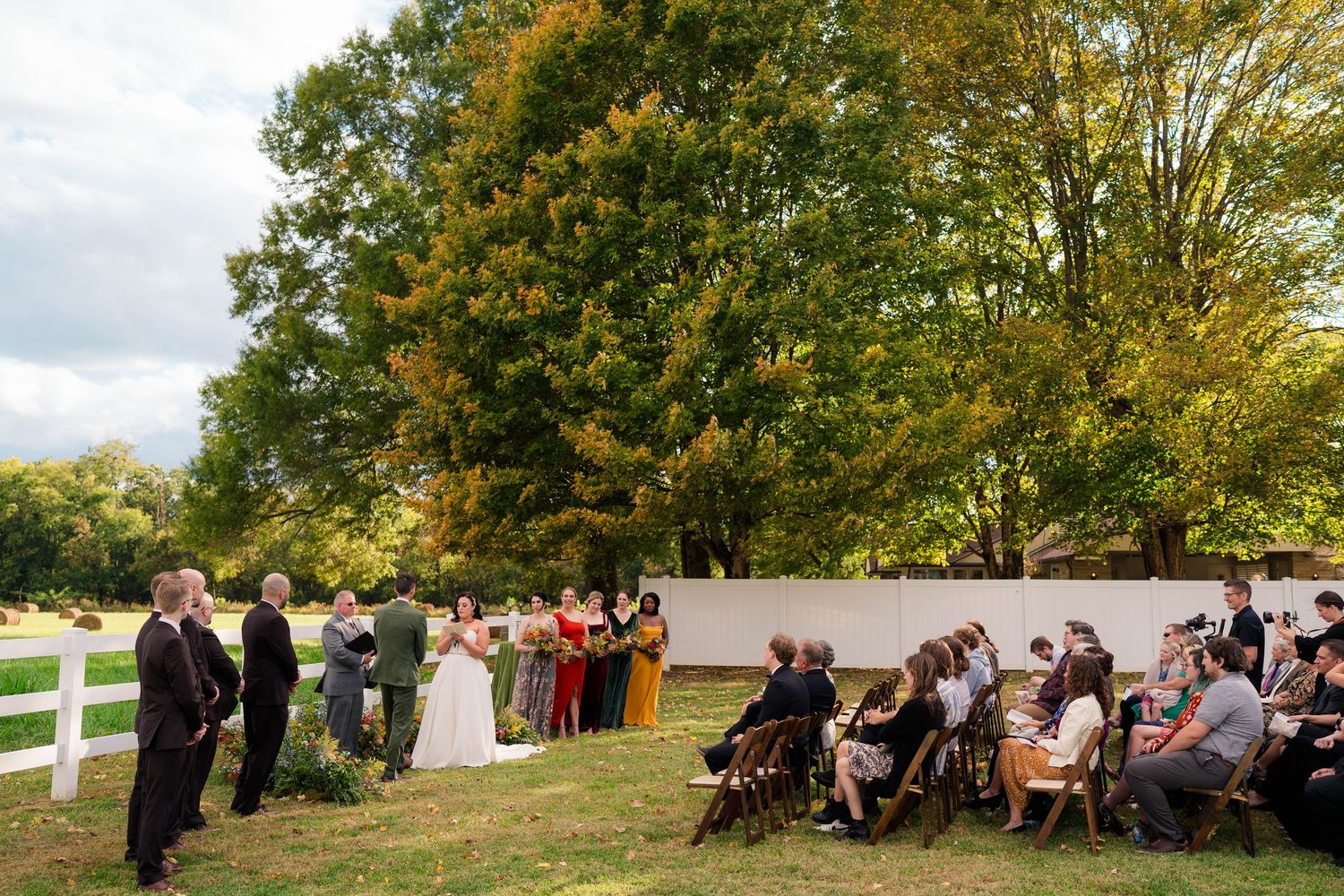 Wide shot of an intimate outdoor fall wedding ceremony with guests seated on a lush green lawn.