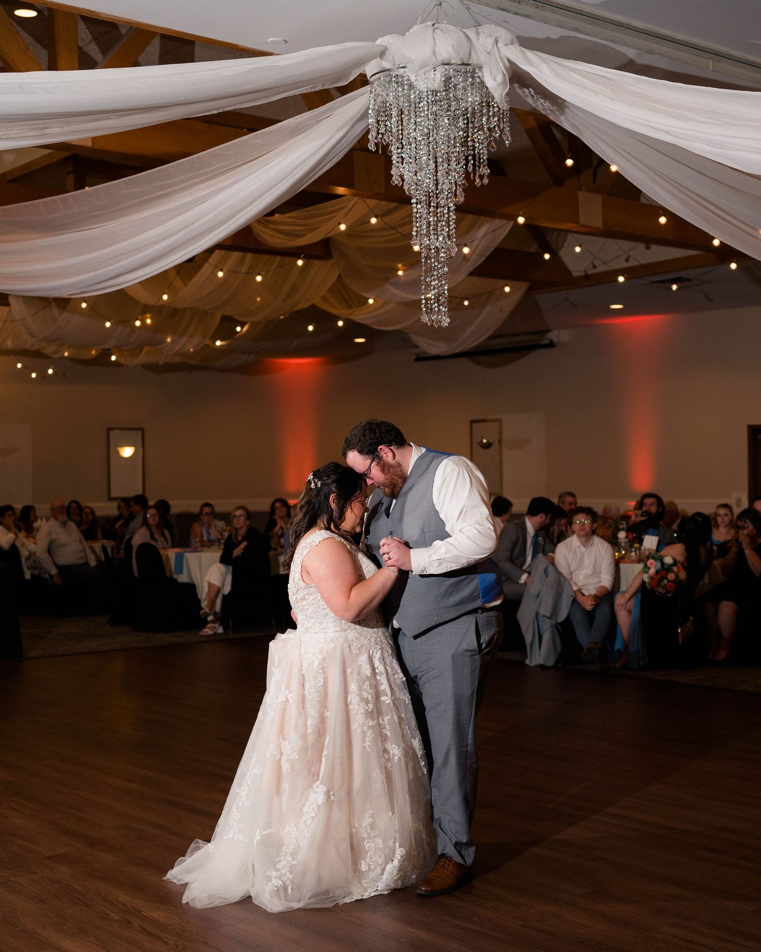Bride and groom share romantic first dance under draped ceiling with twinkling lights.
