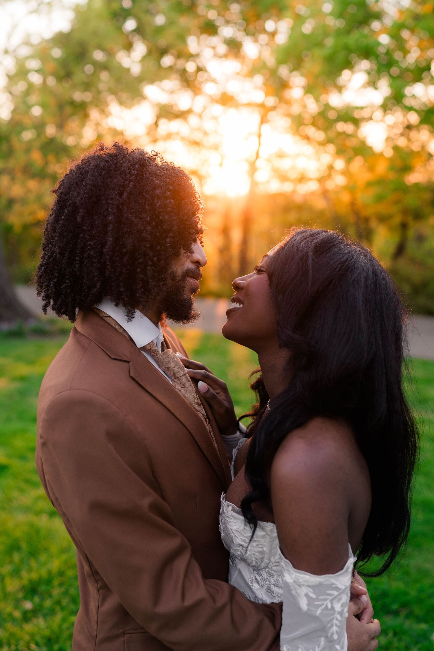 Black couple embraces and laughs together at sunset in wedding attire outdoors.