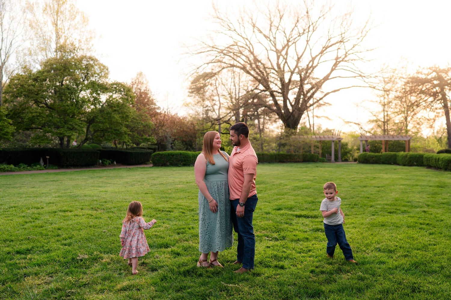 Family of four enjoying a sunny day in a lush green park, parents gazing at each other lovingly.