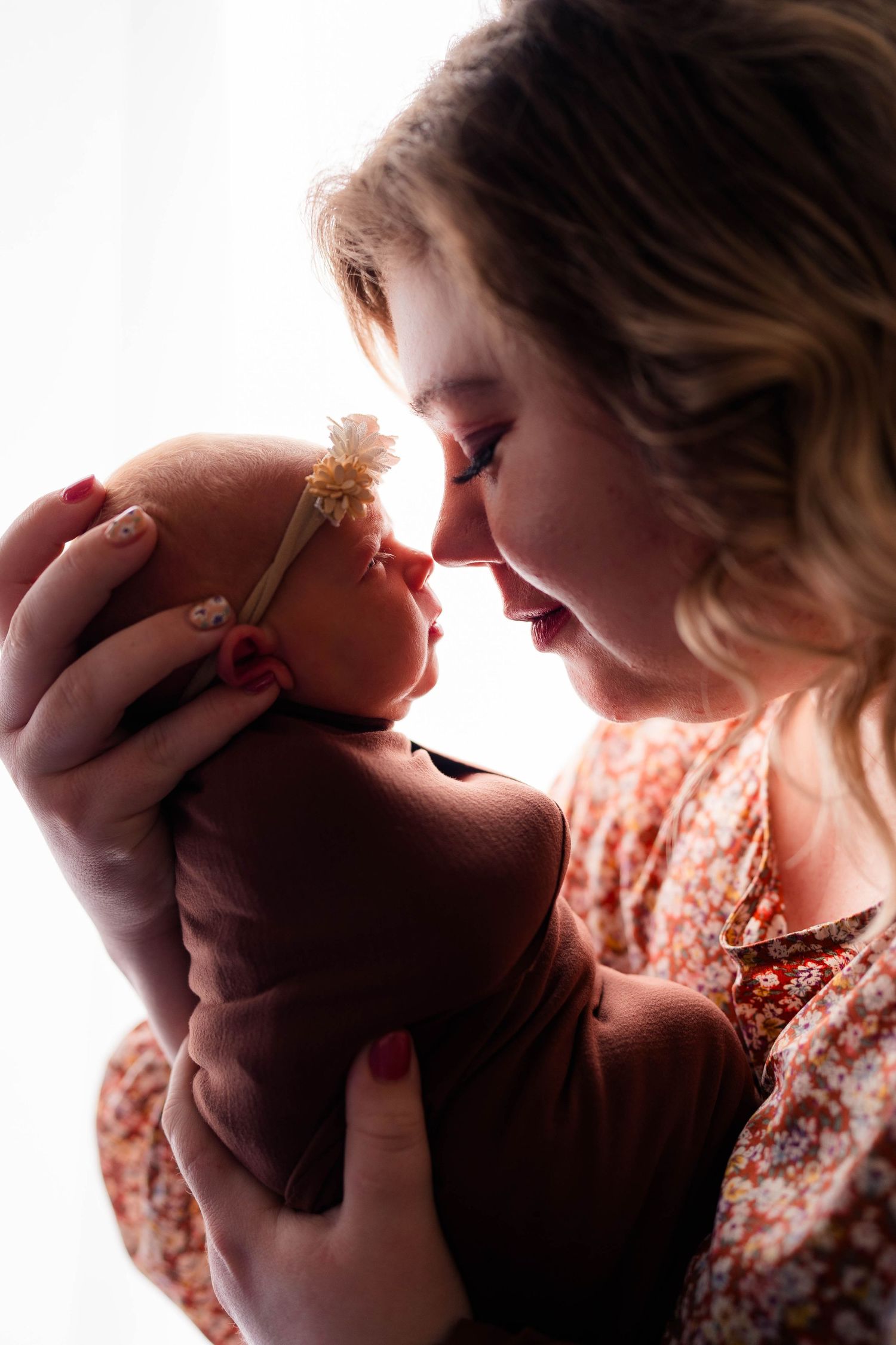 Tender moment of smiling mother holding newborn baby close, touching noses in warm backlight.