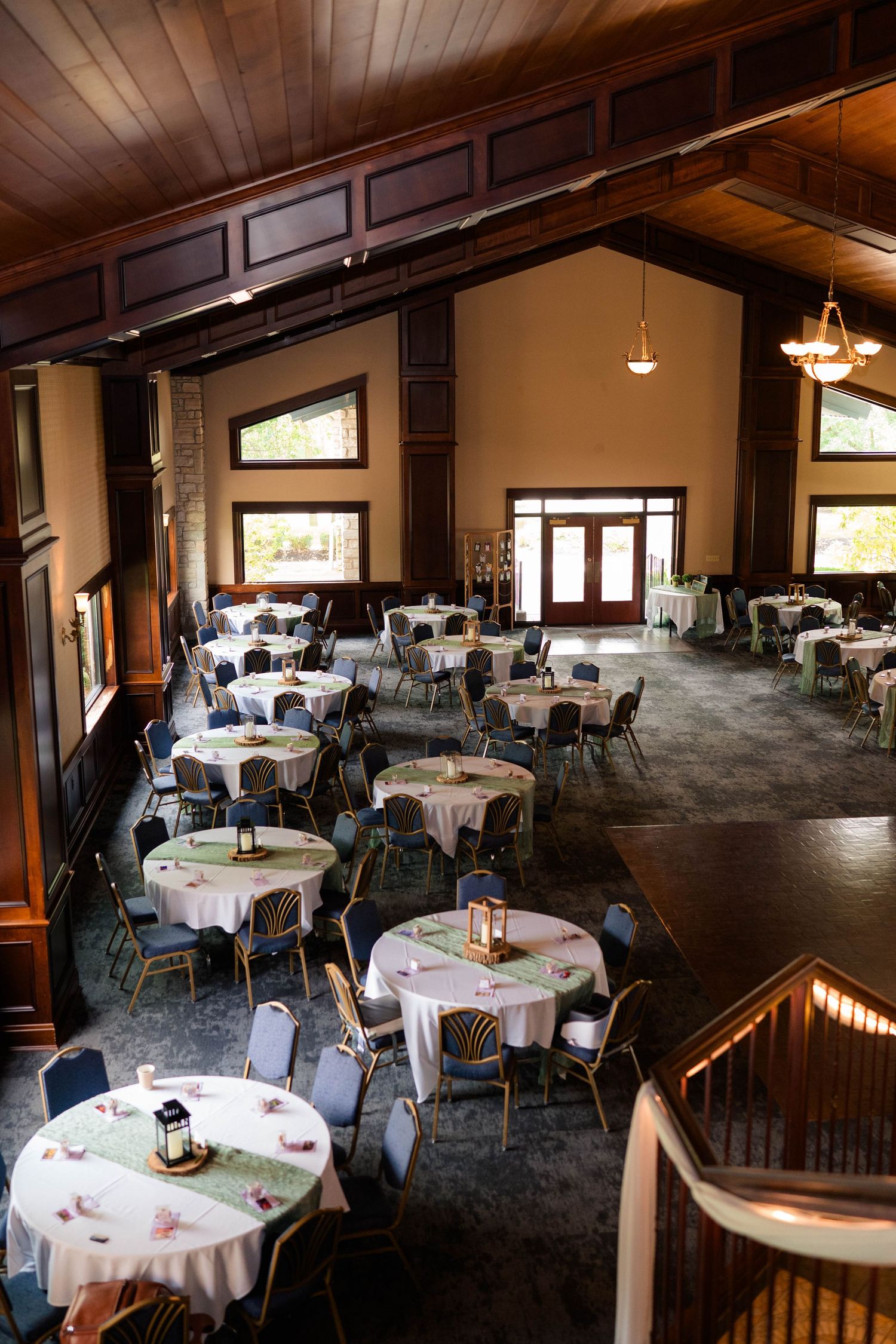Elegant wedding reception hall with round tables set with white linens, lantern centerpieces, and dark wood cathedral ceiling.
