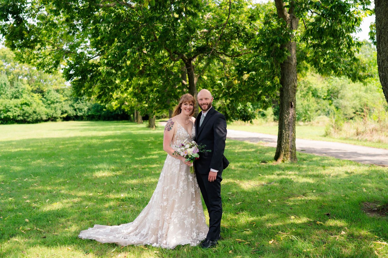 Bride and groom posing together in lush green park on their wedding day.