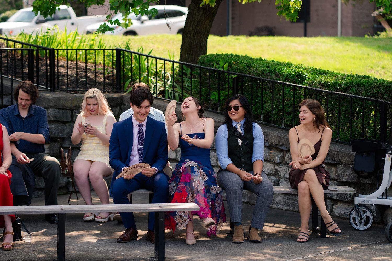 Wedding guests seated outdoors on stone benches enjoying a sunny ceremony.