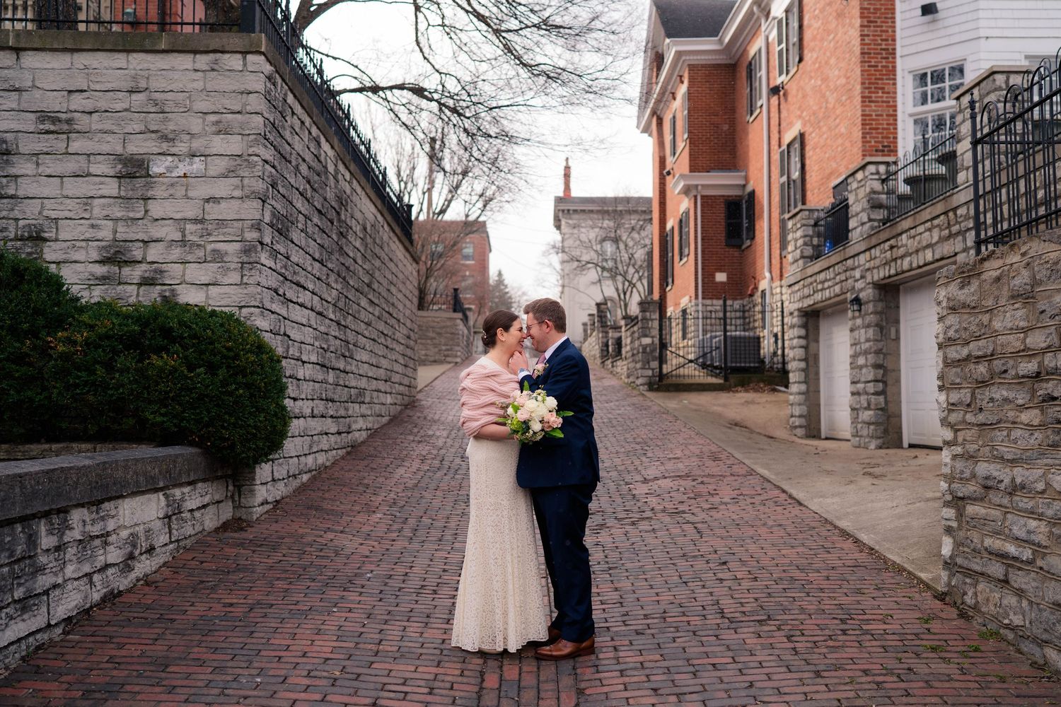 Bride and groom share a romantic kiss on a brick cobblestone alley surrounded by historic brick buildings.