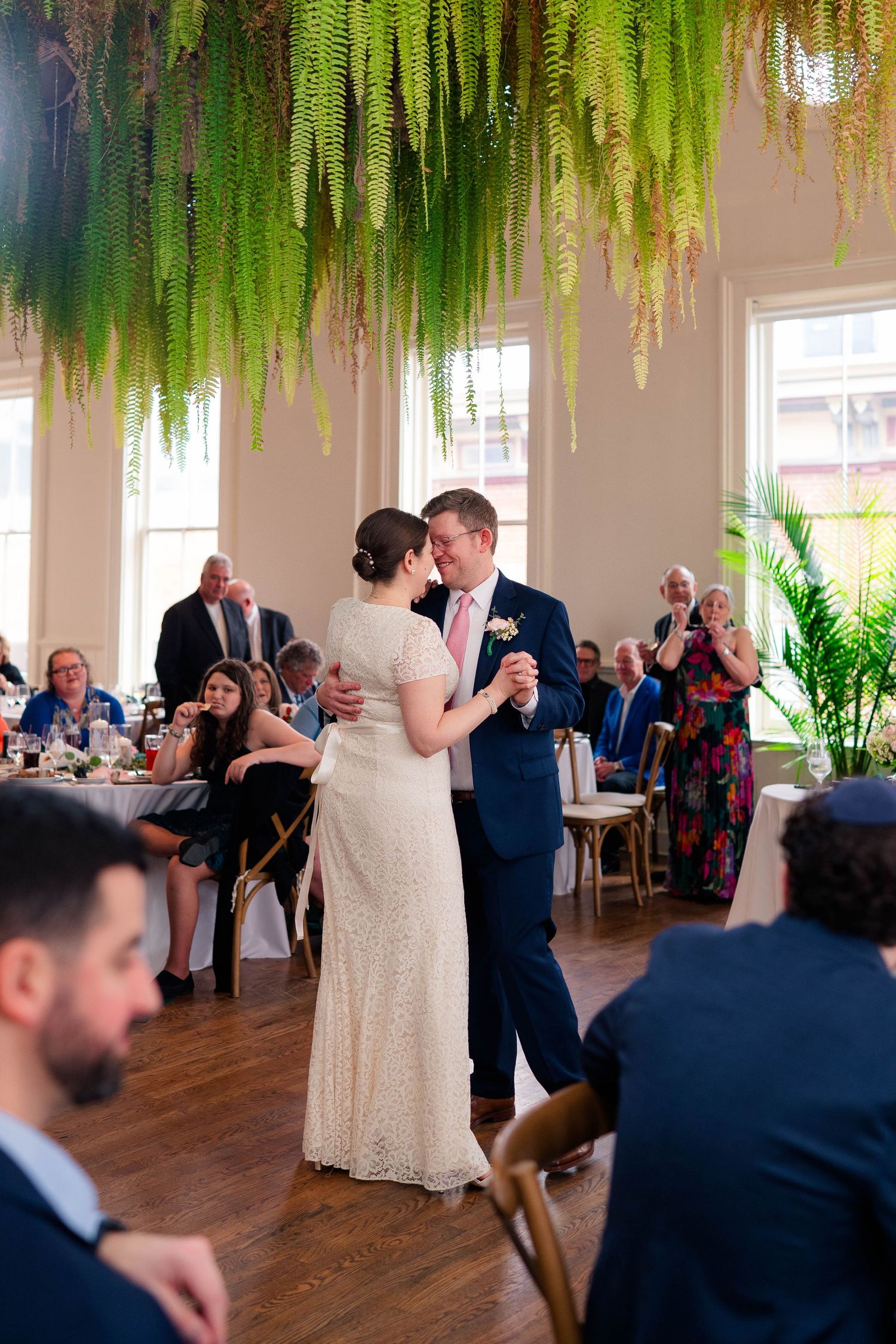Bride and groom dancing together under dramatic hanging fern ceiling at wedding reception.