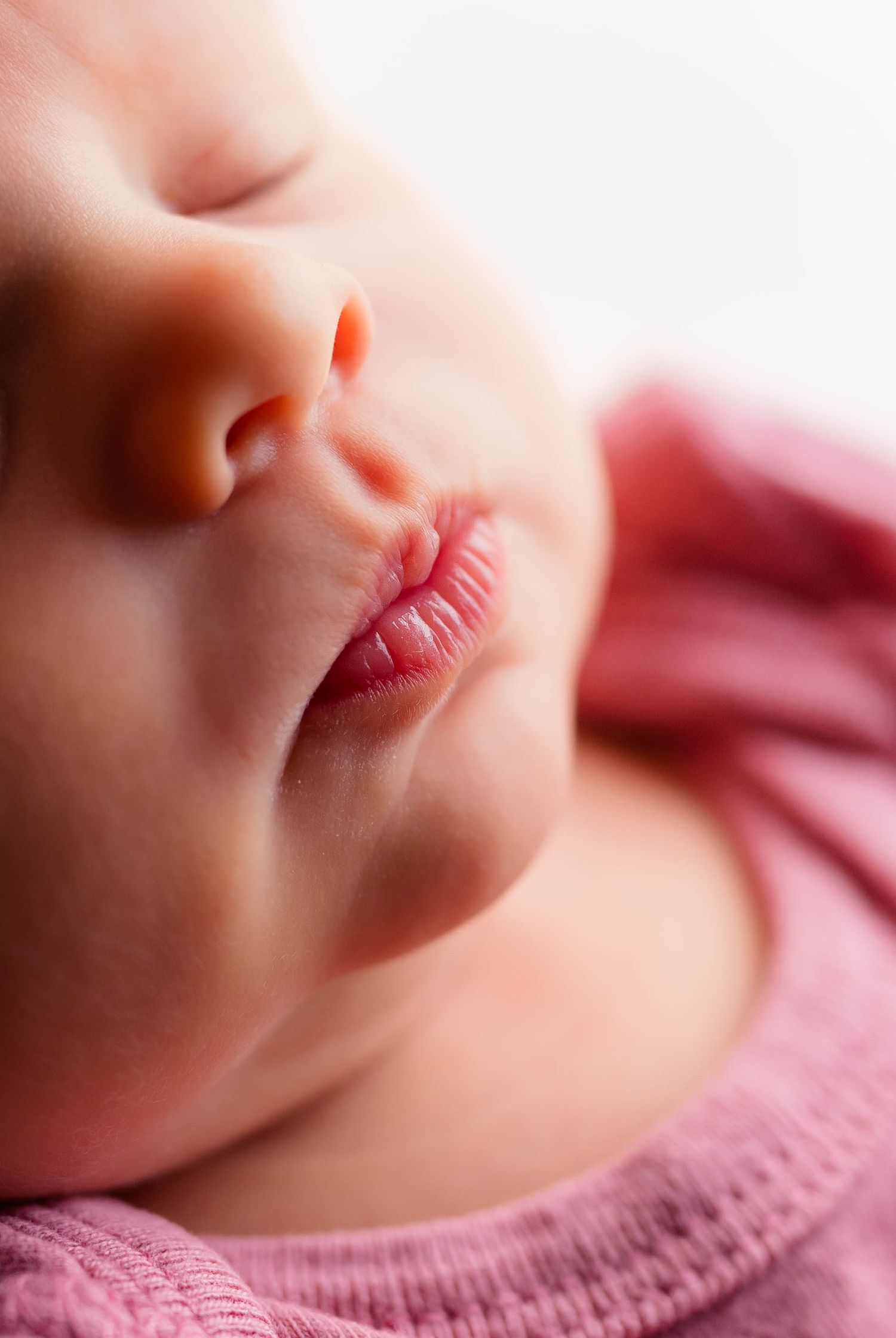 Extreme close-up of peaceful sleeping newborn baby's delicate lips and nose in pink wrap.