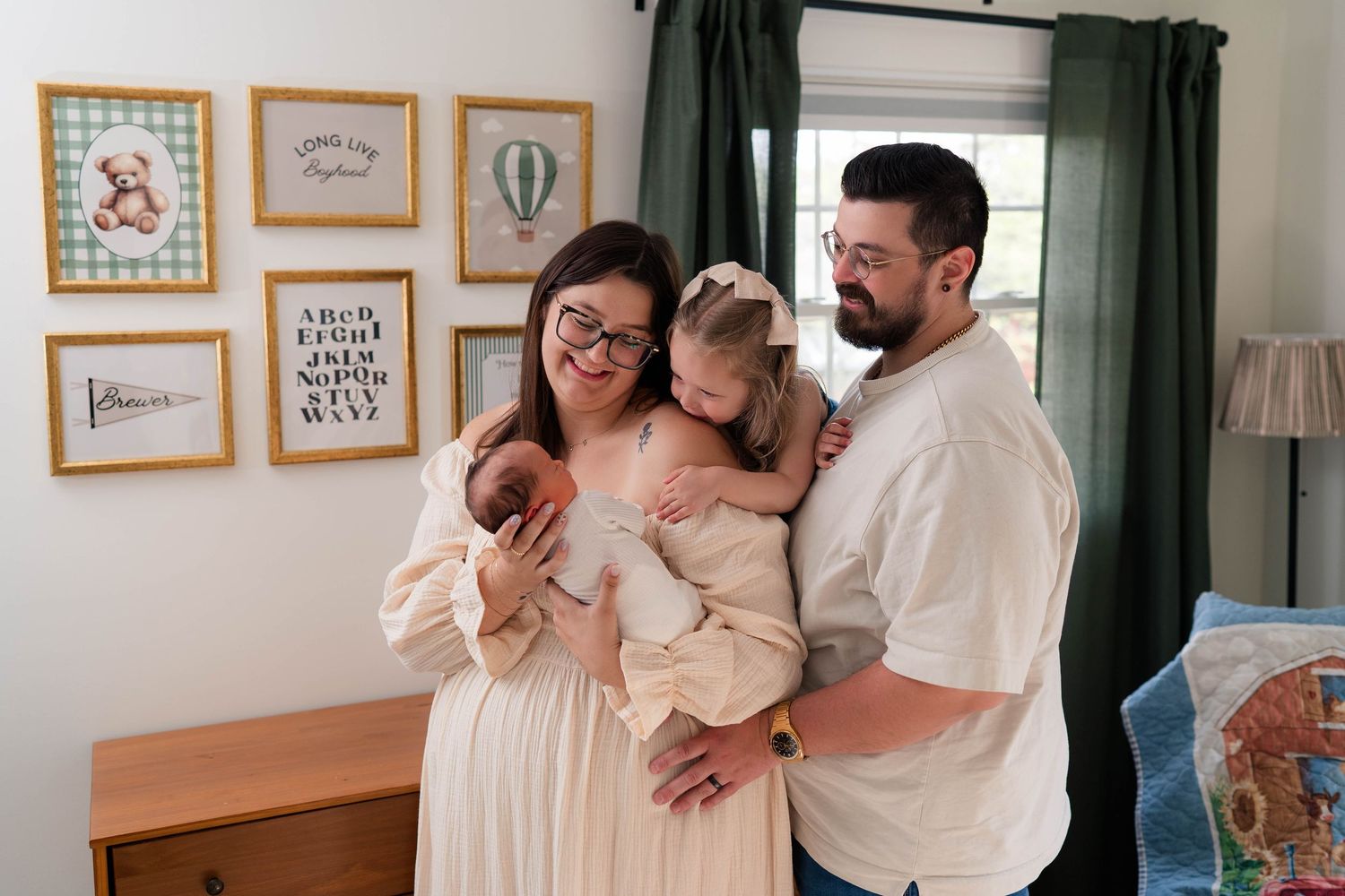Family portrait with parents holding newborn and toddler daughter in a decorated nursery room.