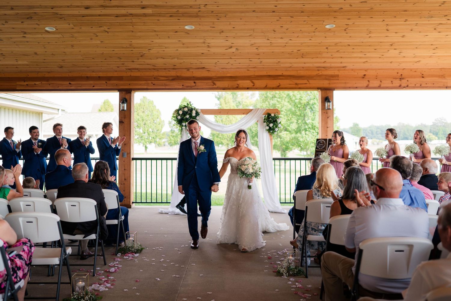 Newlyweds walk back down aisle after wedding ceremony as guests applaud in celebration.