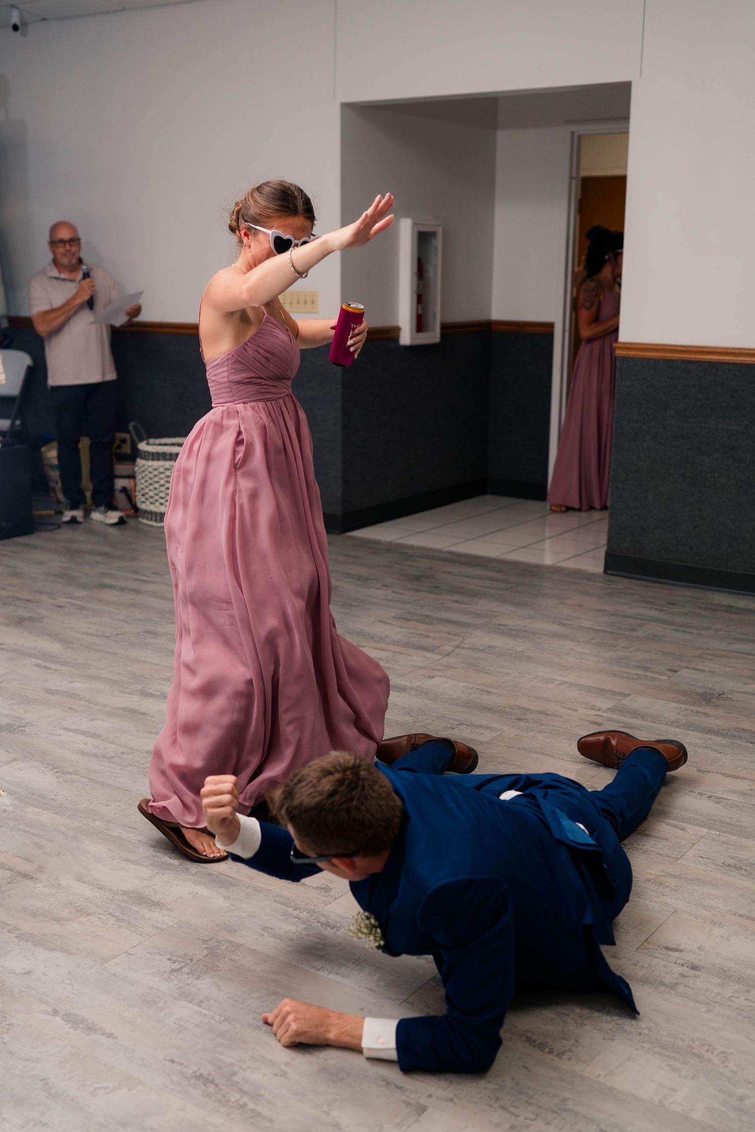 Bridesmaid in pink gown dabbing while groomsman crawls on floor at lively wedding reception dance.