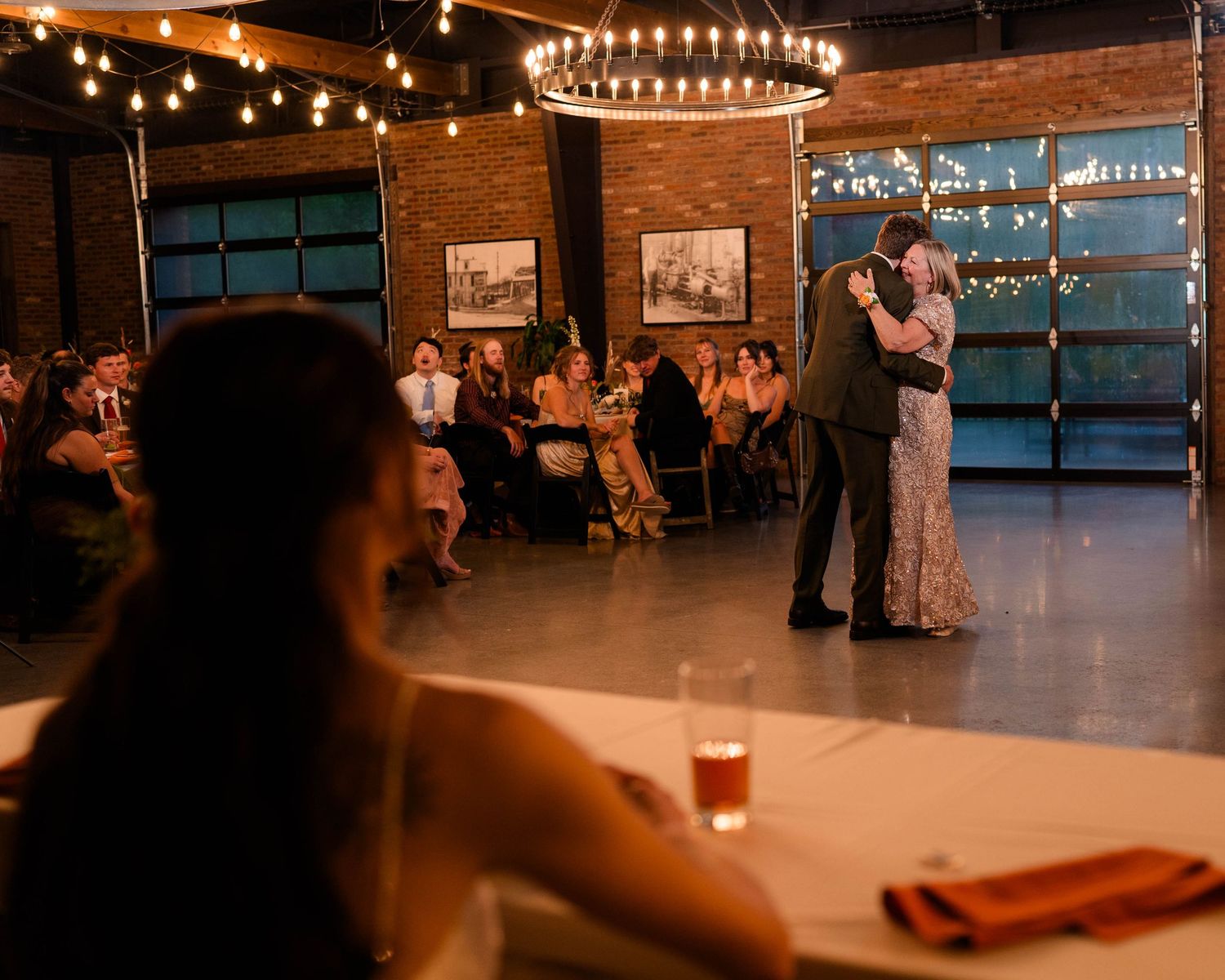 Couple shares first dance on wedding reception floor while guests watch from candlelit tables.