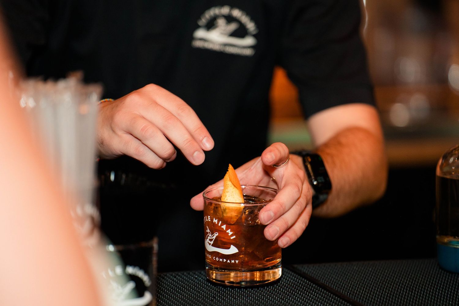 Bartender carefully flames a cocktail garnish over an amber drink in a rocks glass at a wedding reception bar.