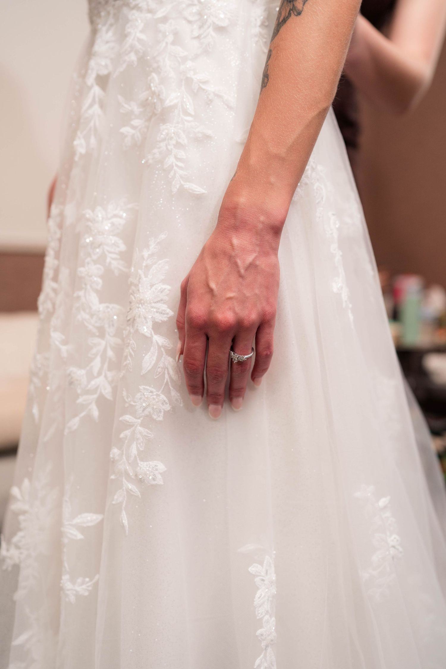 Bride wearing elegant white lace wedding gown displays diamond engagement ring on her hand.