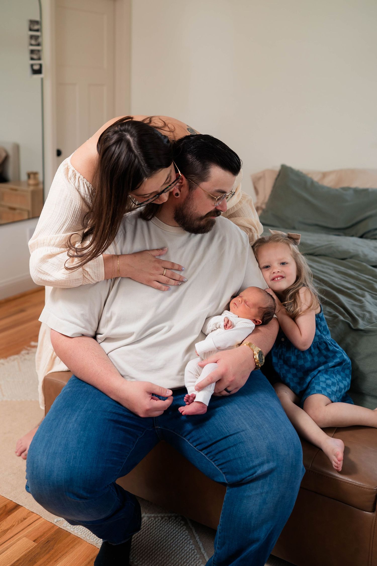 Family of four with newborn baby and toddler daughter sharing a tender moment together indoors.