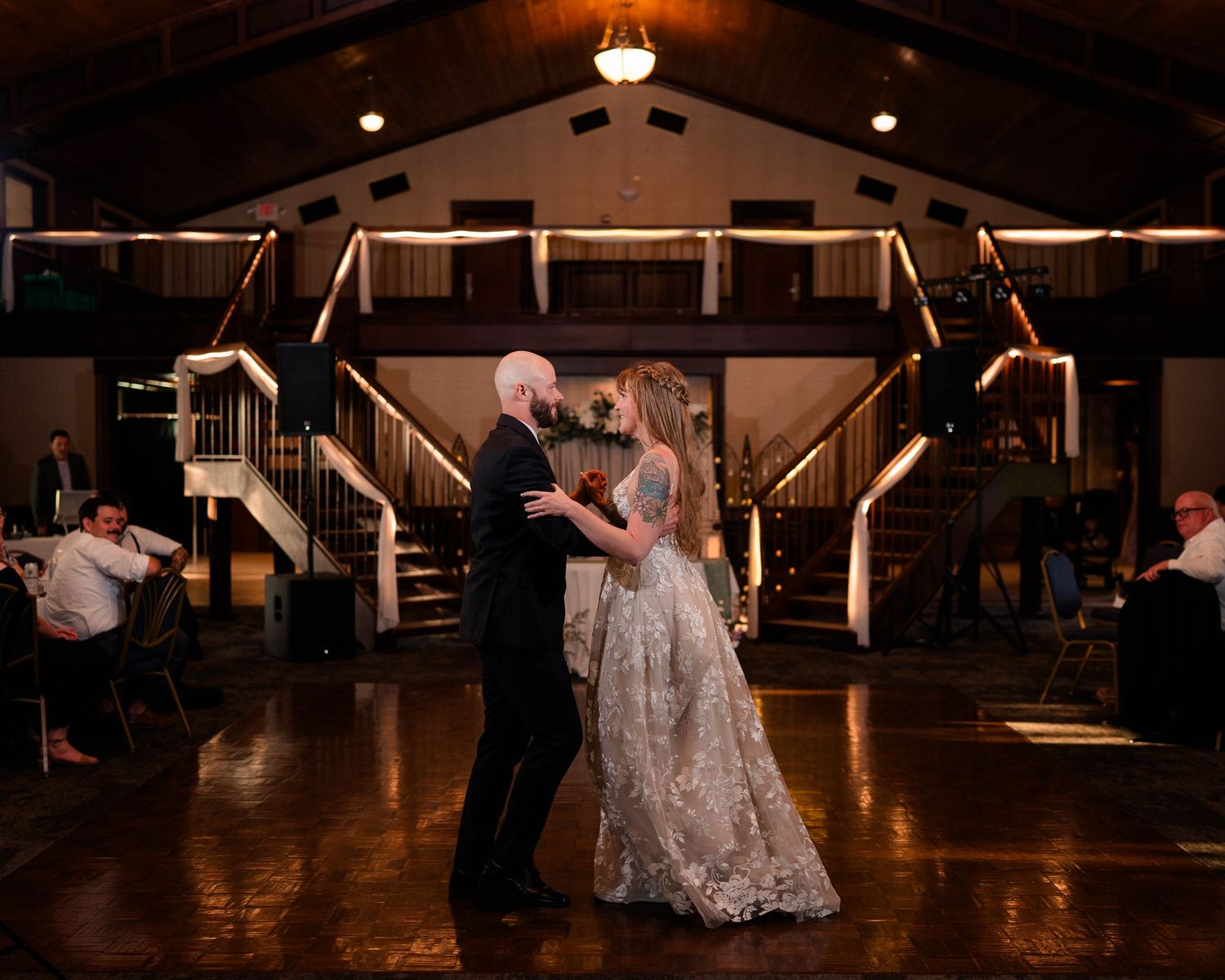 Bride and groom share first dance on dimly lit dance floor in rustic wedding venue.