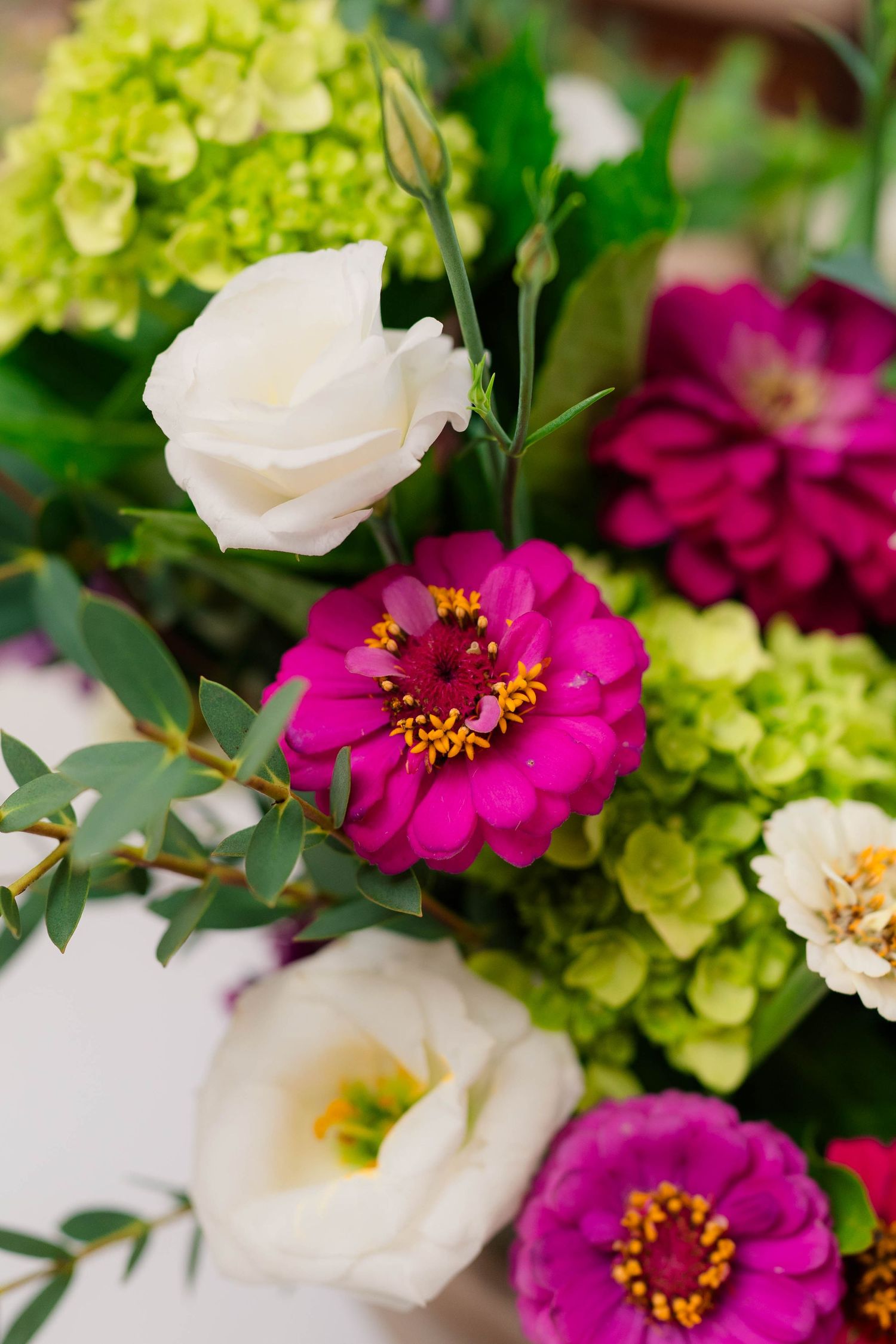 Vibrant wedding floral arrangement featuring magenta zinnias, white roses, and green hydrangeas.