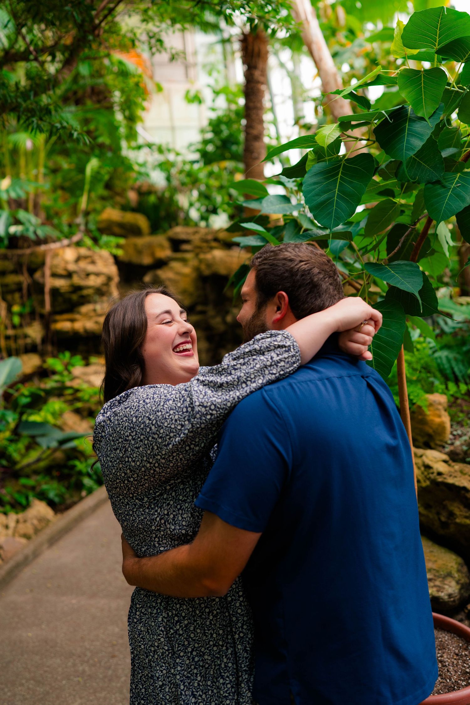 Newly engaged woman laughs joyfully while embracing her fiance in a lush tropical botanical garden.