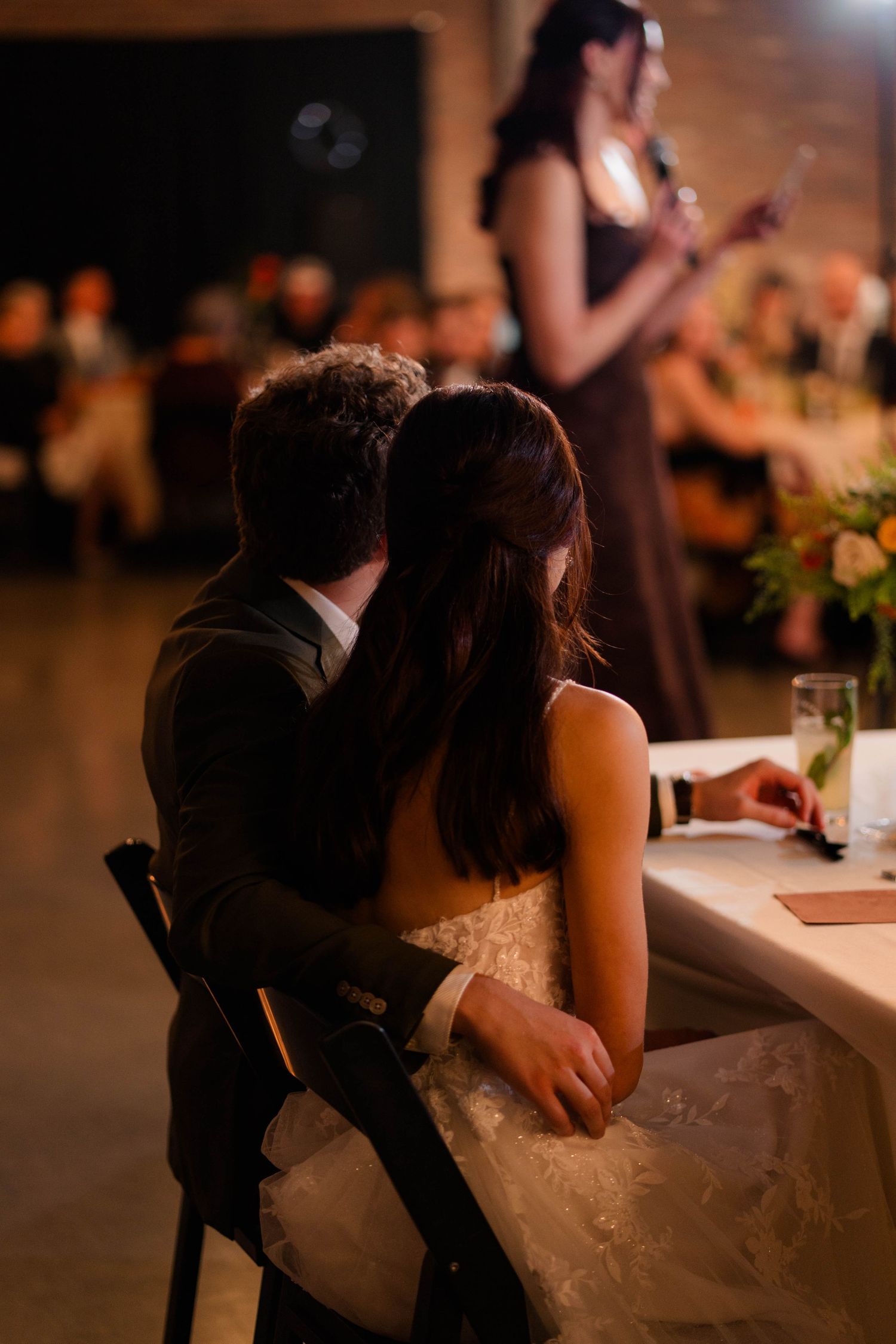 Bride and groom seated together at sweetheart table during wedding reception performance.