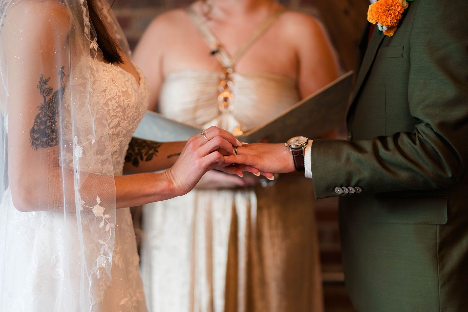 Close-up of bride and groom exchanging rings during wedding ceremony with officiant in background.